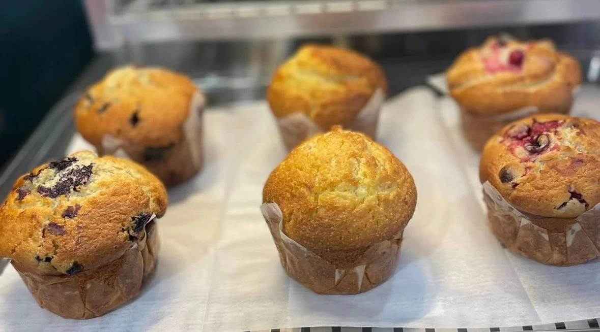 Six freshly baked muffins on a parchment-lined tray, some with blueberries and others with raspberries.