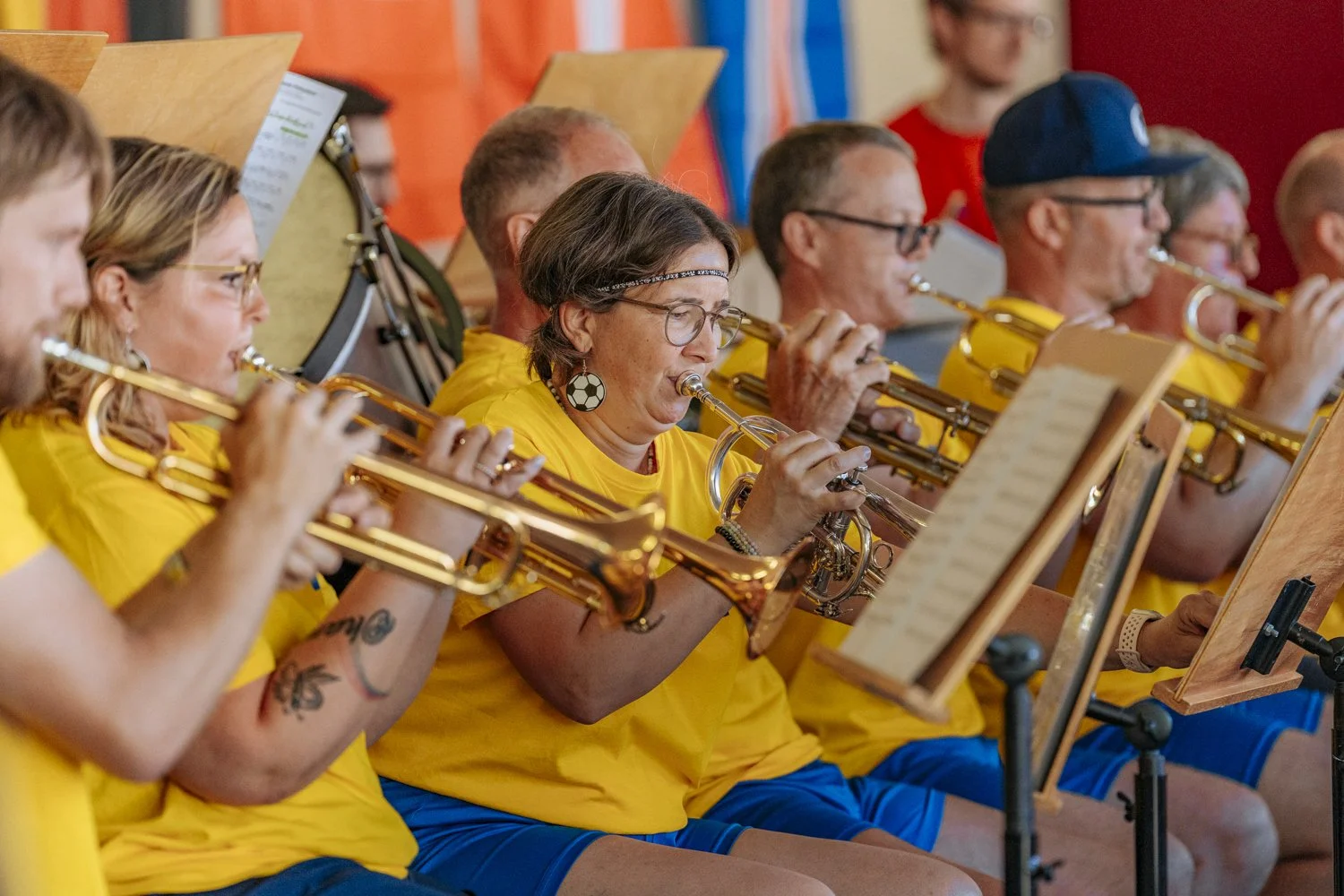 Eine Gruppe von Musikern in gelben T-Shirts spielt Trompeten in einem Orchester, während sie Noten lesen.