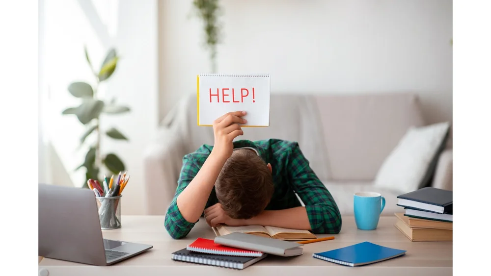 Overwhelmed student at a desk holding a sign that says HELP