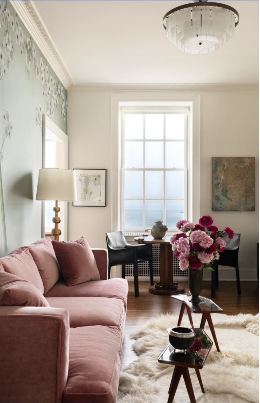 Sitting room with hand-painted floral walls, rose velvet sofa, sculptural tables, and a vintage French game table by the window.