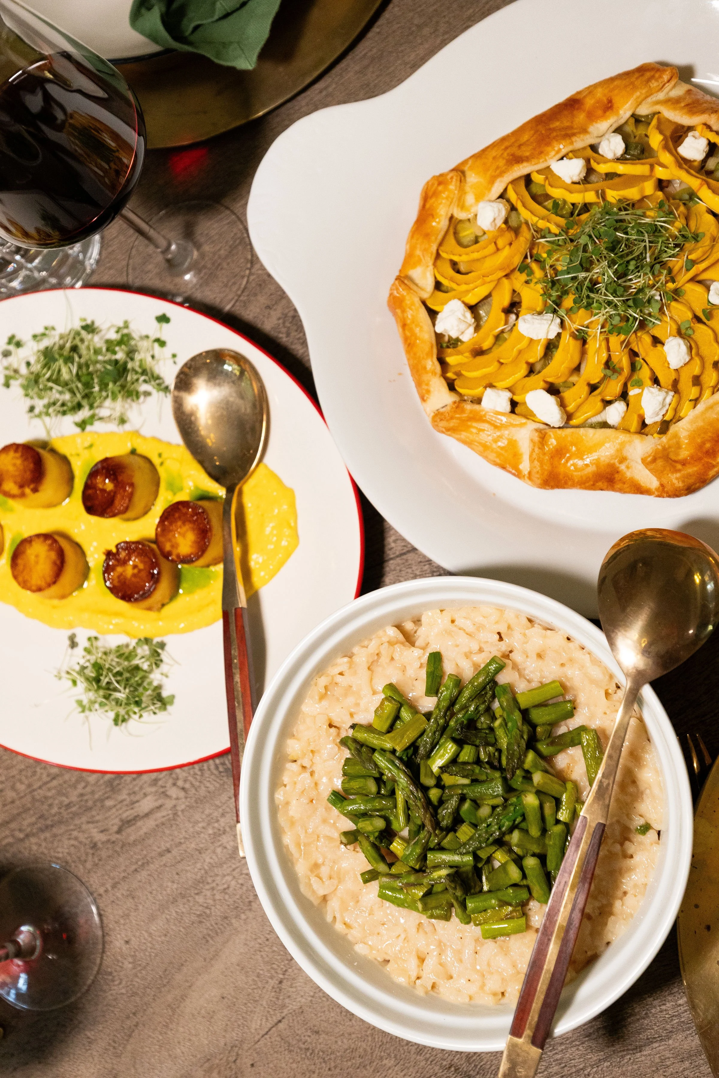 food on a table including potato scallops and a delicata squash tart with a wine glass