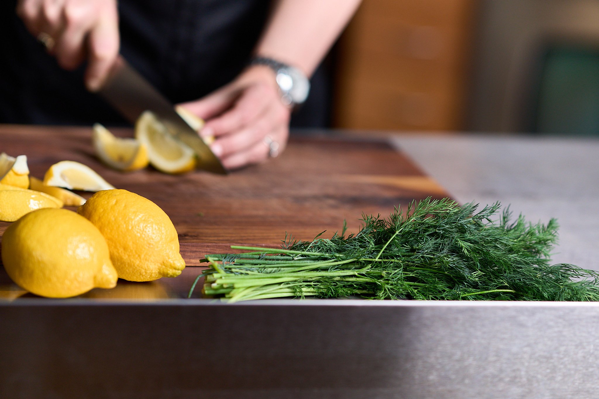 Chef cutting lemons on a wood cutting board with dill in front