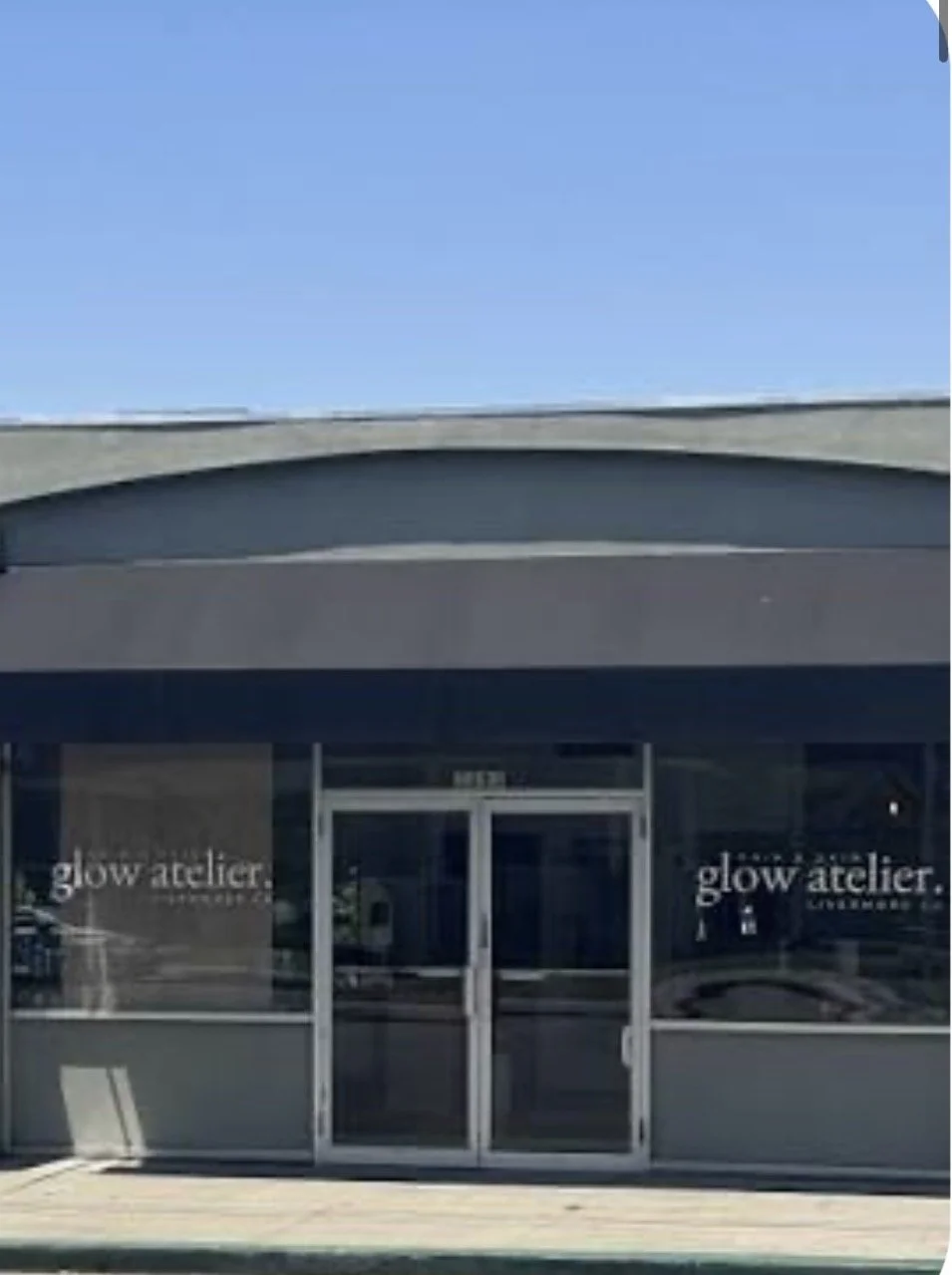 Exterior view of a storefront with glass doors and windows, signage reading 'glow atelier' on both sides of the entrance, and a neighboring business sign on the left.