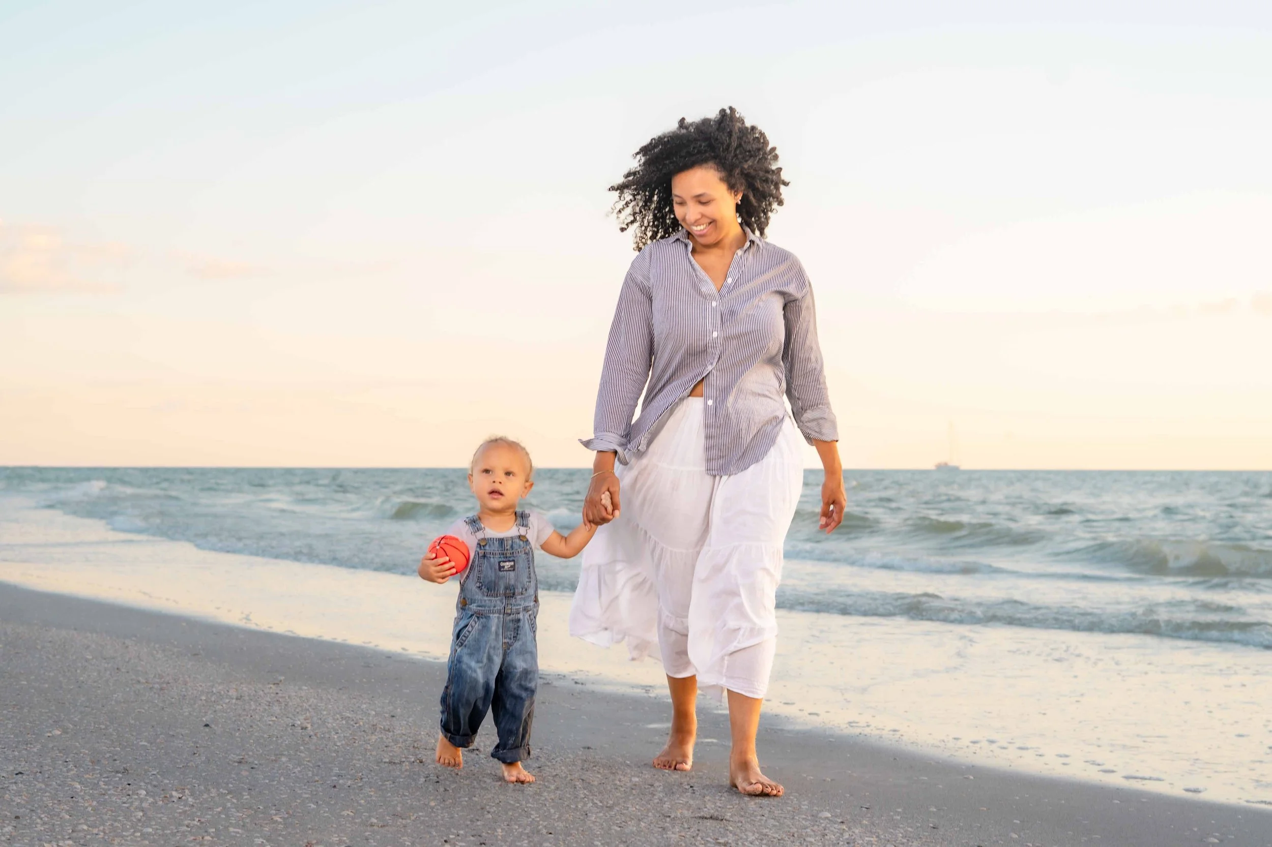 Mom holding hands with toddler on St. Pete Beach at sunset
