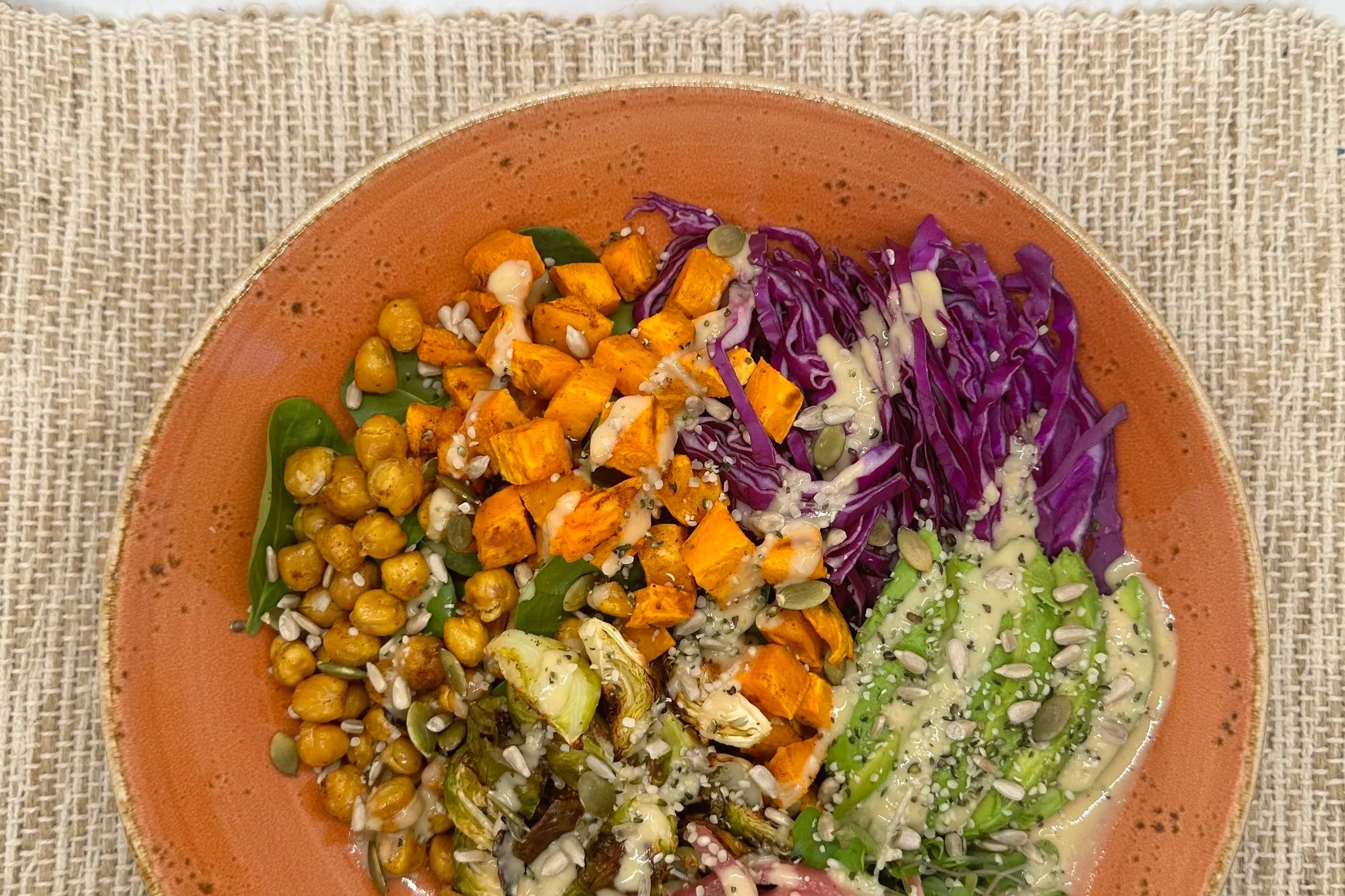 Grain bowl of quinoa, spinach, roasted sweet potatoes and brussel sprouts, red cabbage and avocado, drizzled with tahini and TOP'T seed mix