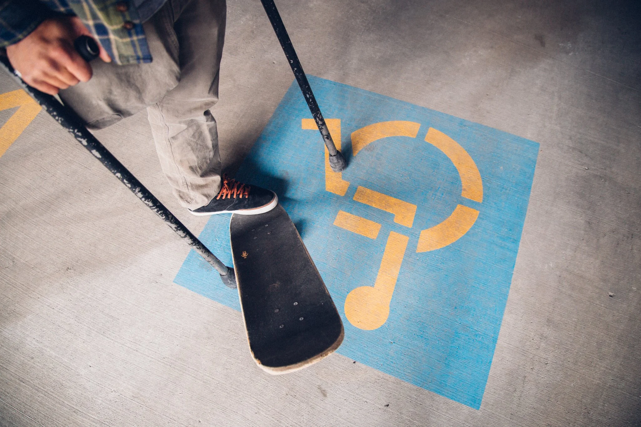 Vasu' lower body standing on the tail of a skateboard over a accessible parking logo