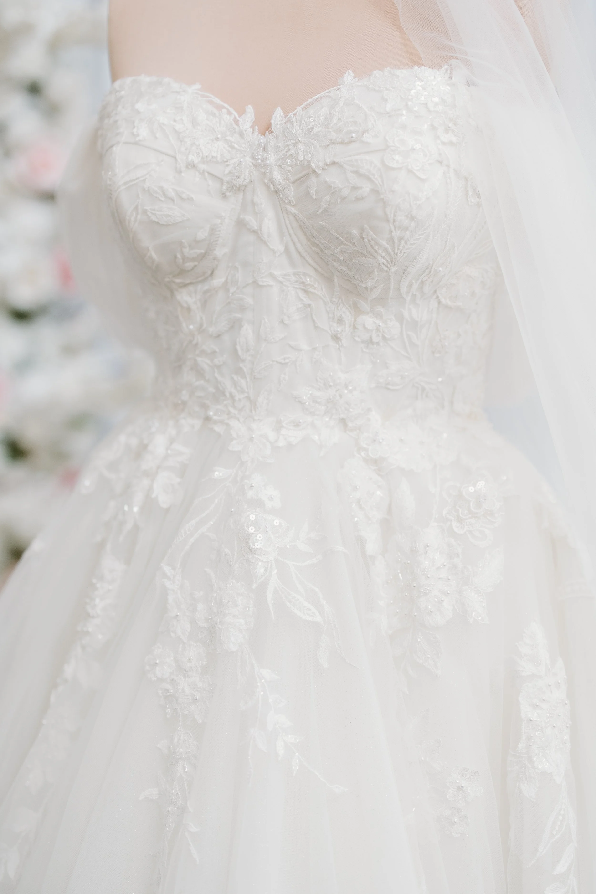Close-up of an elegant white wedding dress with intricate lace and floral embroidery, featuring a strapless sweetheart neckline.