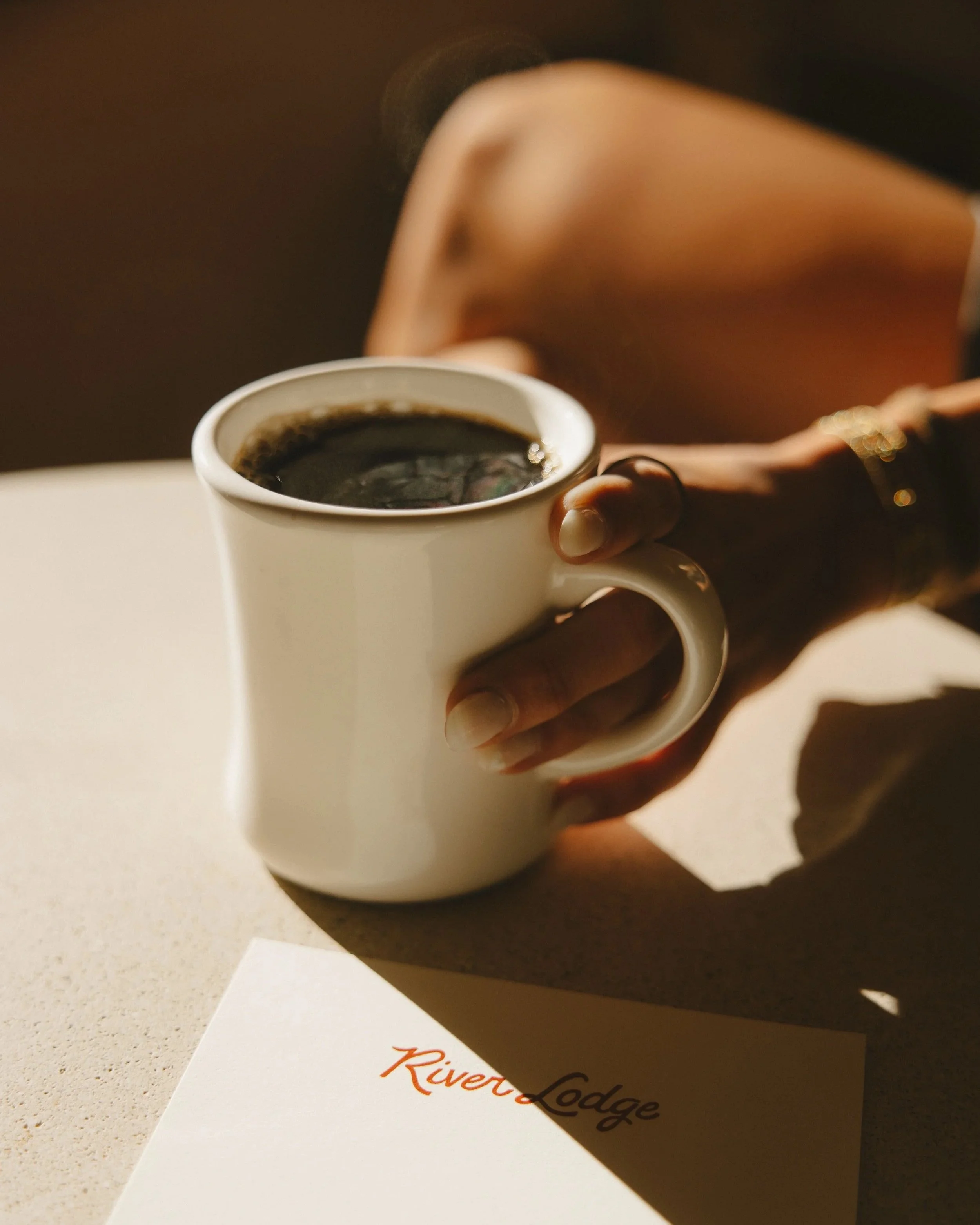 A person holding a white mug filled with black coffee.