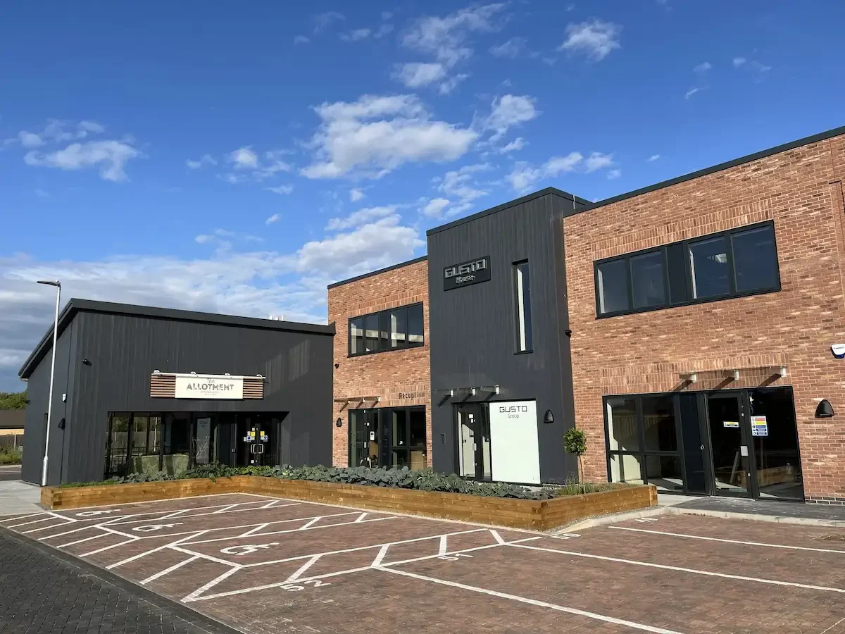 Building named 'GUSTO House' next door to The Allotment Cafe and Deli in Collingham. In front of the building is an empty car park.