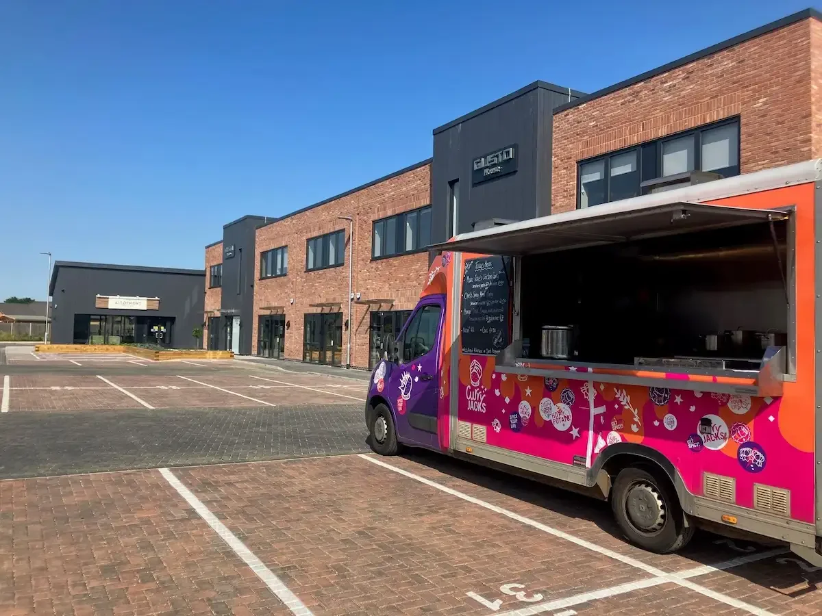 A pink and purple van serving curry and Indian in an empty car park at Gusto House