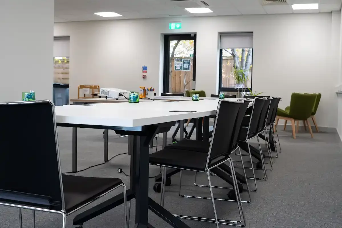 White tables and black chairs set up in a U-shaped layout, mints are on the table and a projector