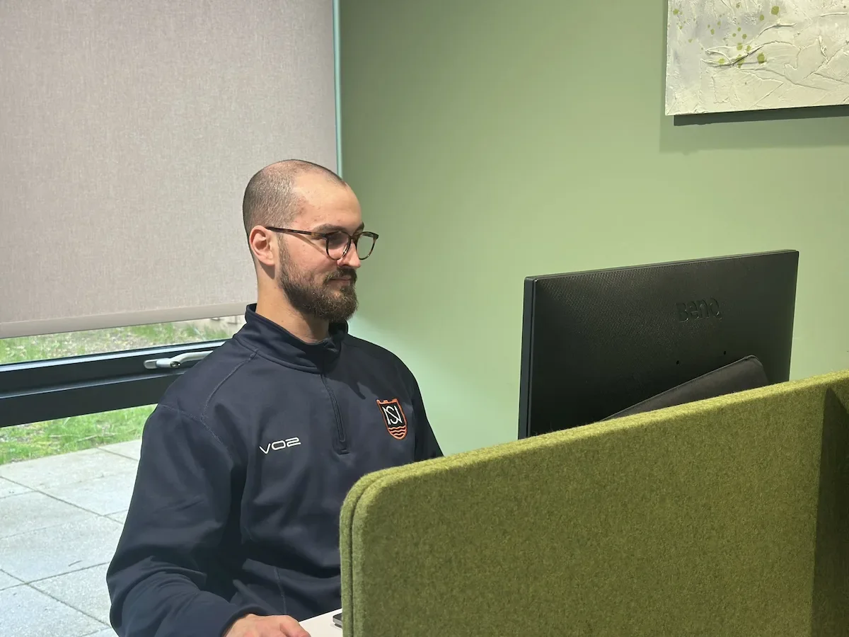 A man with glasses sat looking at a computer screen in a green coworking space