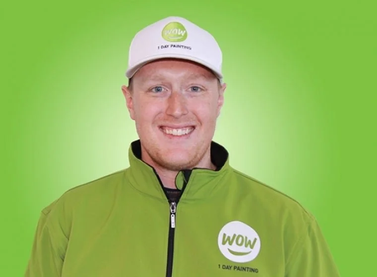 Smiling man wearing a white cap and green jacket with 'WOW 1 DAY PAINTING' logo, standing against a green background.