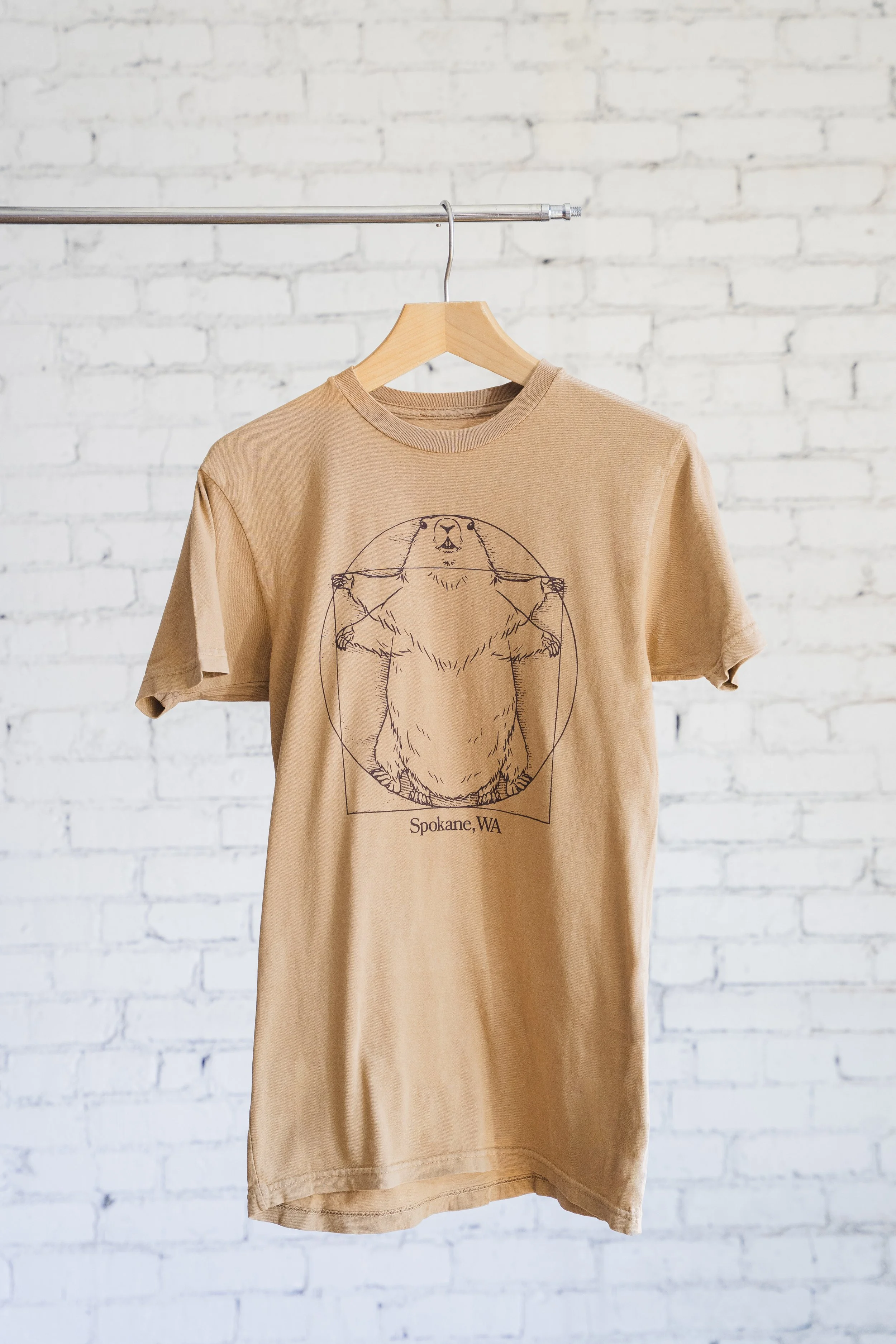 brown shirt with hand drawn vitruvian marmot design in front of white brick wall