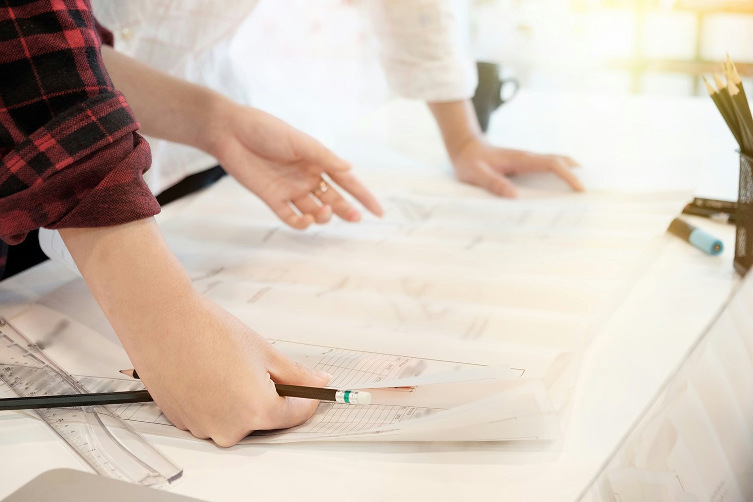 two people lean over house drawings while holding pencils and rulers