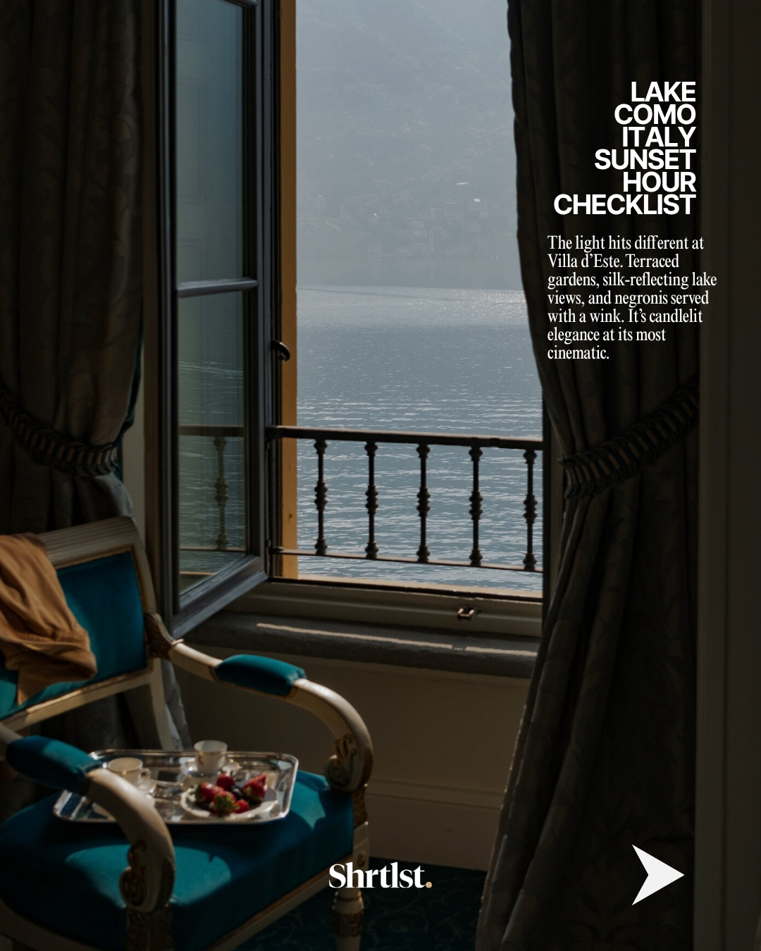 A partially open window with curtains revealing a view of Lake Como at sunset, with a chair and a tray with strawberries and cups in the room.