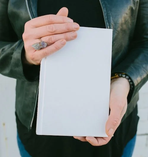 woman in a black jacket holding a blank white book