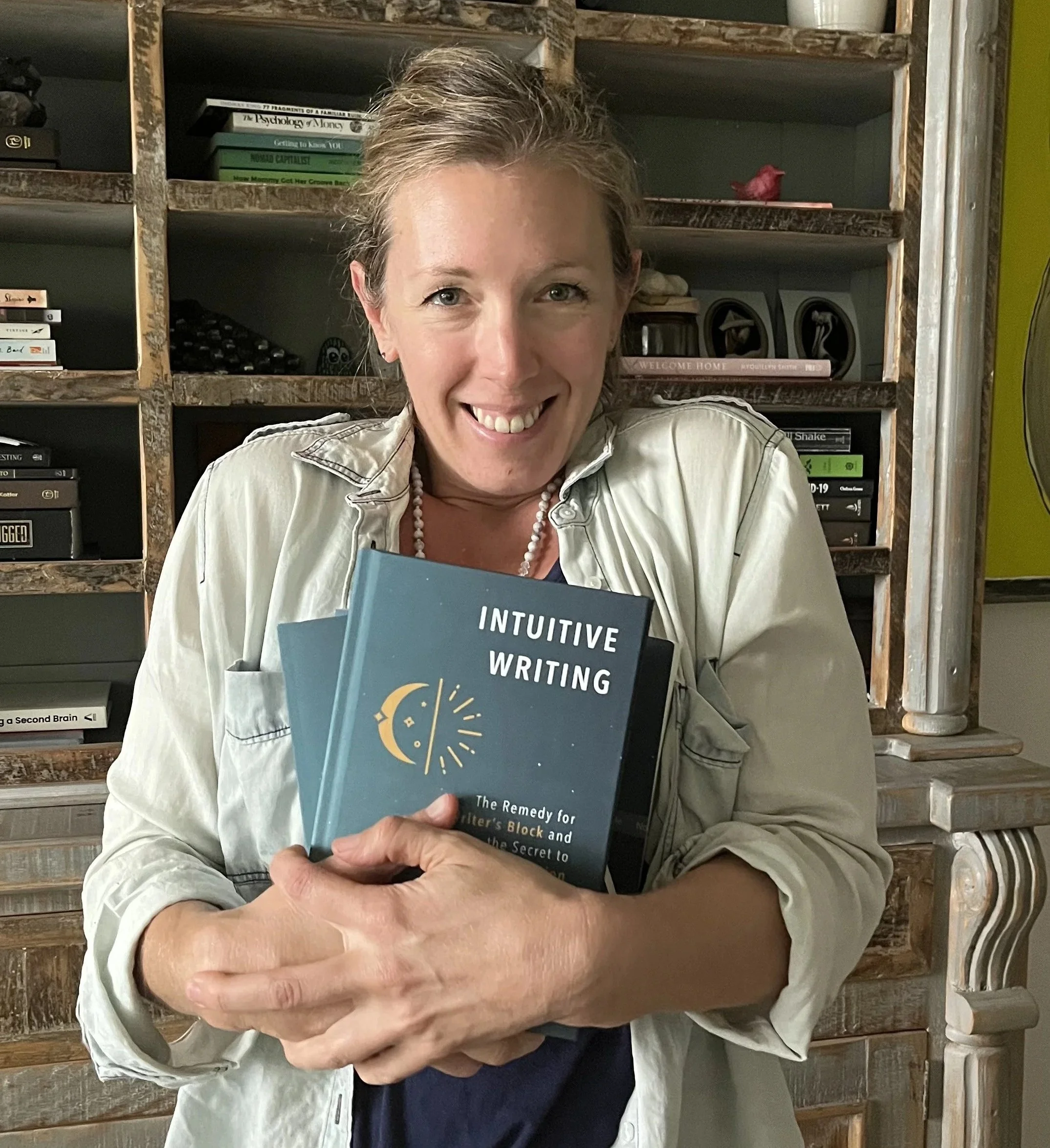 Jacqueline Fisch, author, in a denim shirt holding a bundle of hardcover books, Intuitive Writing