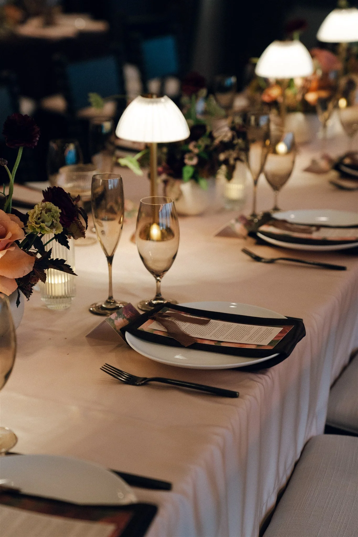 Elegant table setting with plates, cutlery, remembrance candles, wine glasses, and floral centerpieces, illuminated by small lamps.