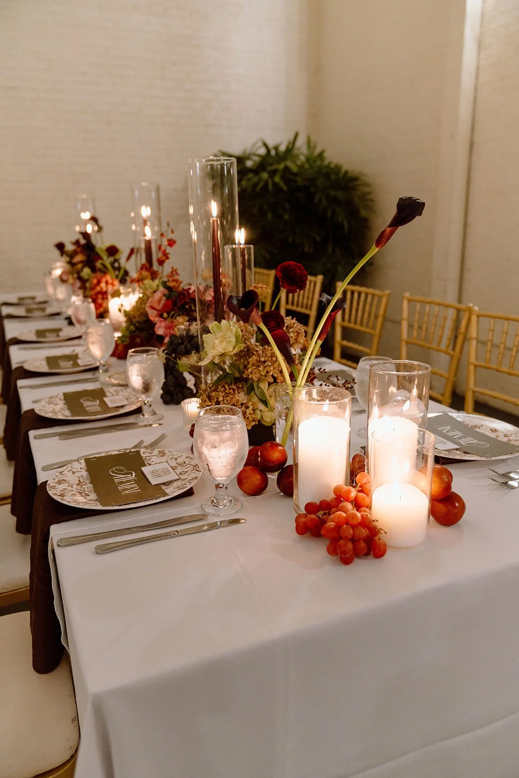Elegant banquet table decorated with flowers, tall candles, grapes, and apples, set for a formal event.