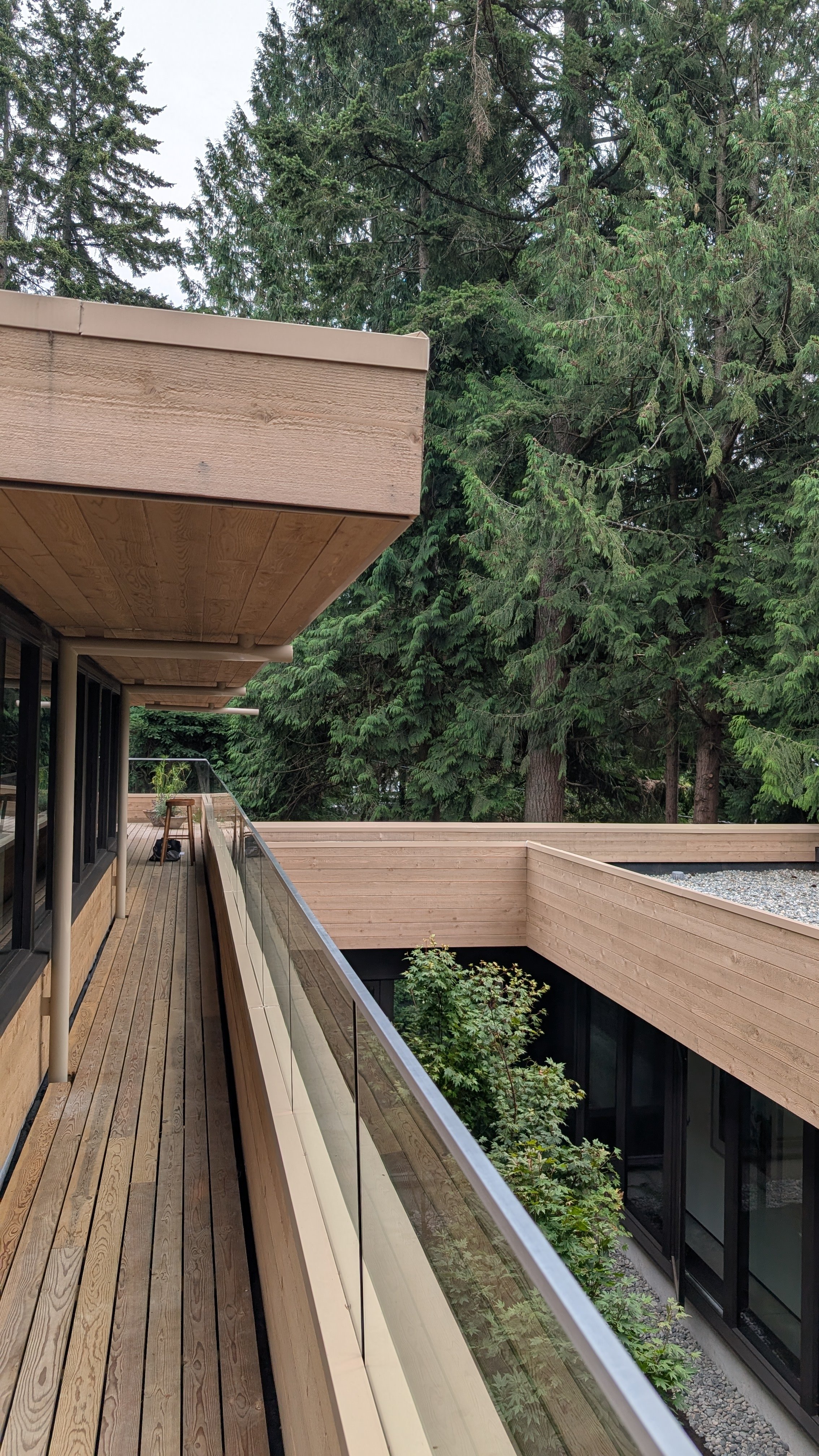 View from a modern balcony with wooden flooring and glass railing overlooking trees and a multi-story building.