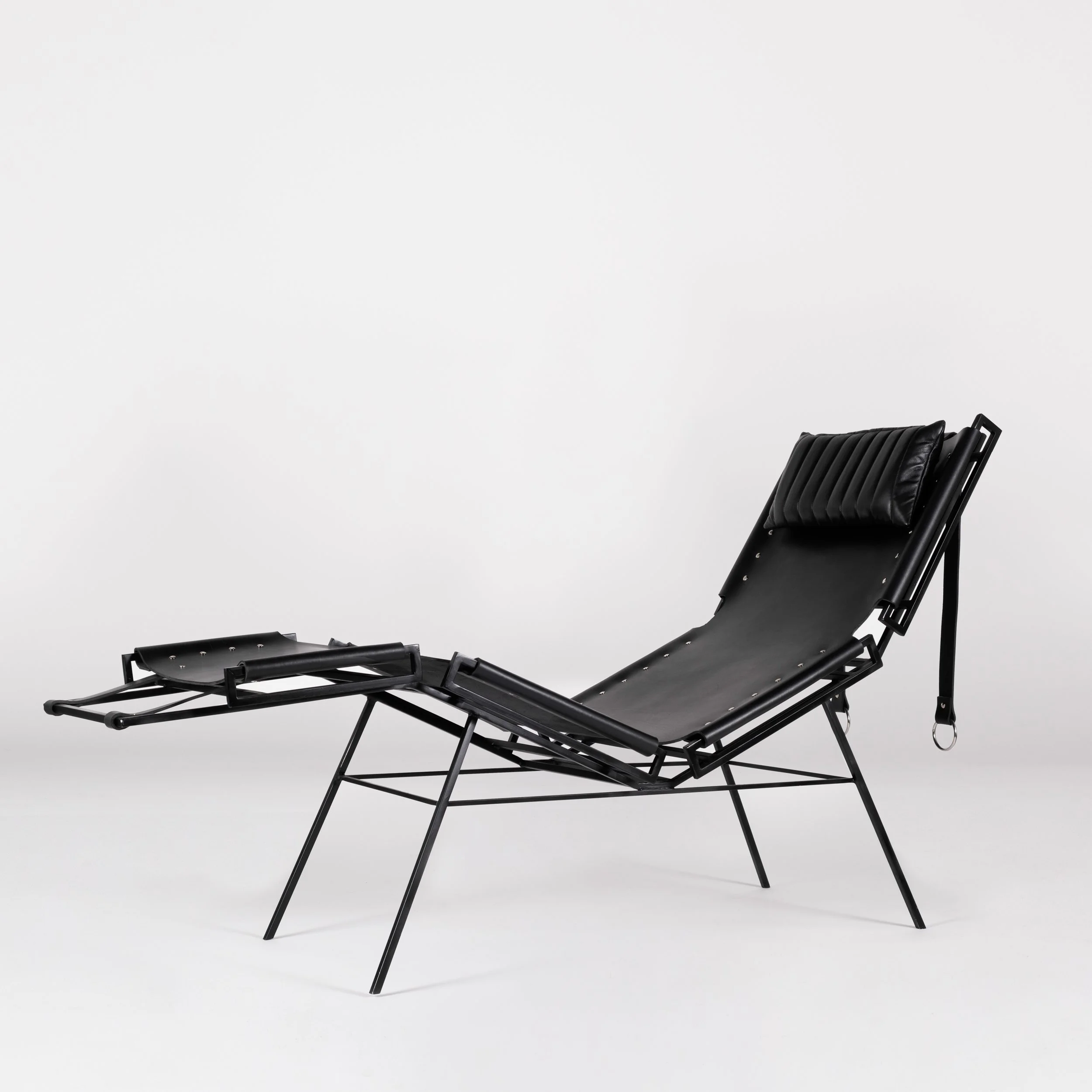A black leather lounge chair with adjustable headrest, made of metal frame, set against a plain white background.
