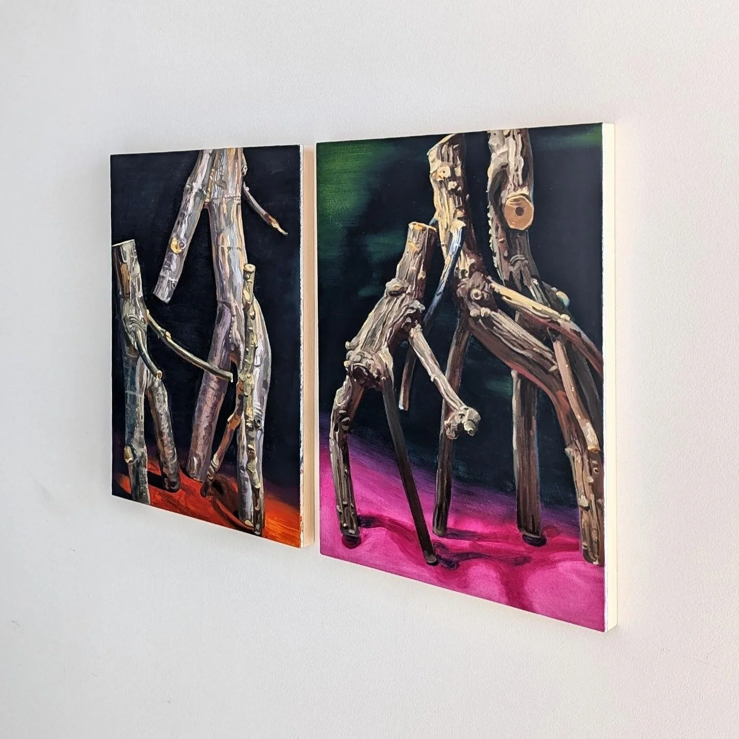 Two paintings of abstract trees made of wood logs, with colorful backgrounds, hung on a white wall.