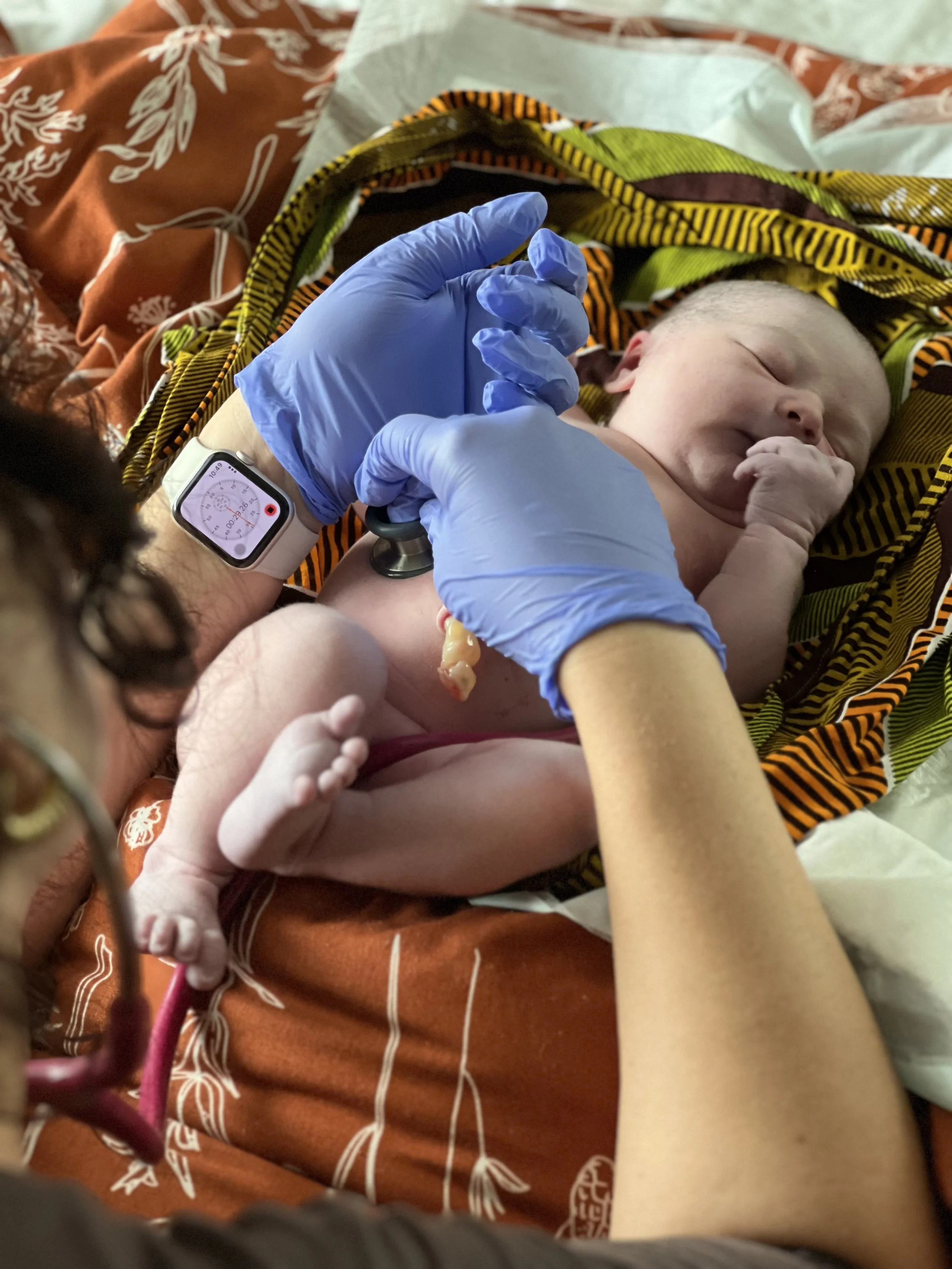 A newborn baby lying on a colorful blanket, getting a medical checkup from a healthcare professional