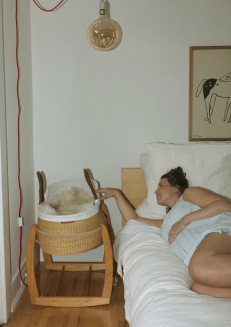 Close-up of a baby lying on a soft blanket, wearing a white long-sleeve shirt, with one hand near their face and their thumb near their ear.