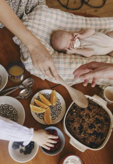 Close-up of a sleeping baby lying on a white blanket, with one hand resting near their head and wearing a white long-sleeve shirt.
