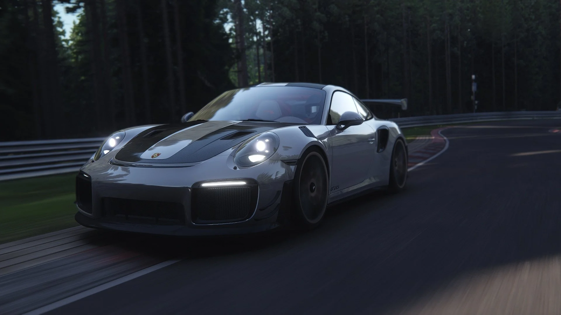 A silver Porsche 911 GT2 RS race car on a racetrack surrounded by trees, with its headlights on and a rear wing.