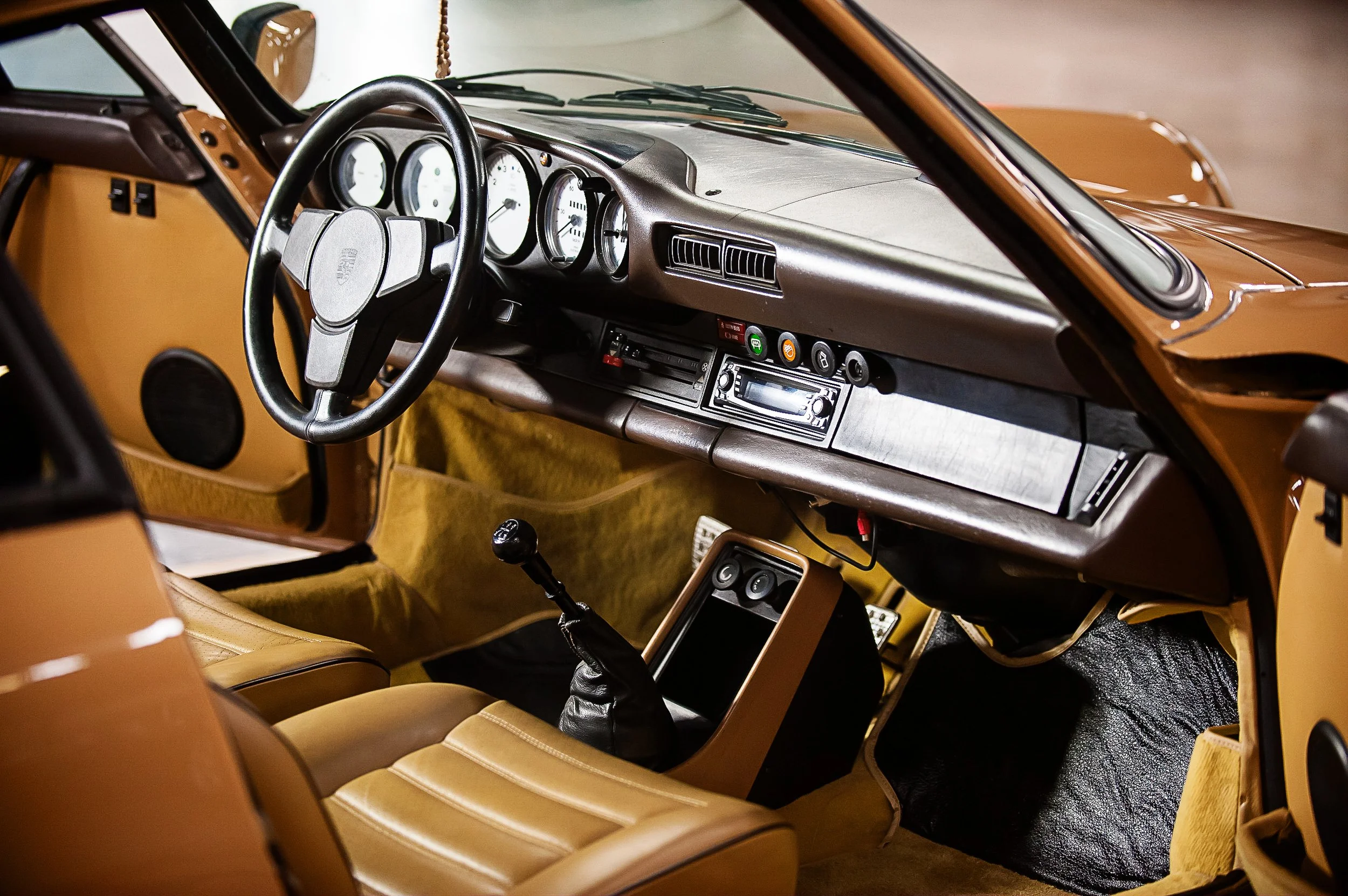 Interior of a vintage car showing a brown dashboard, steering wheel, gauges, audio system, and tan seats.