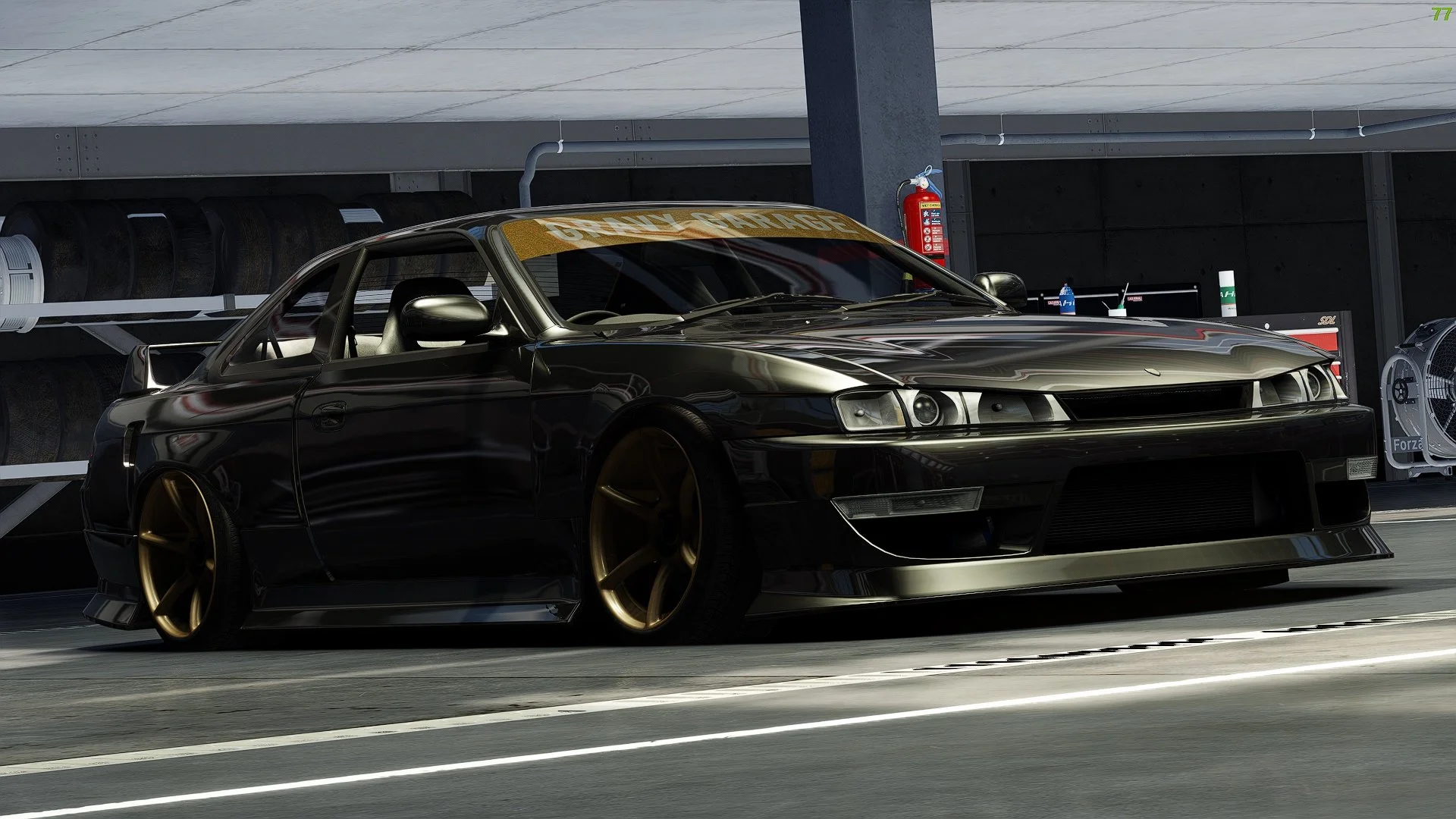 Black race car with gold wheels parked in a garage, with a sign reading 'GRR ONLY GARAGE' on the windshield.