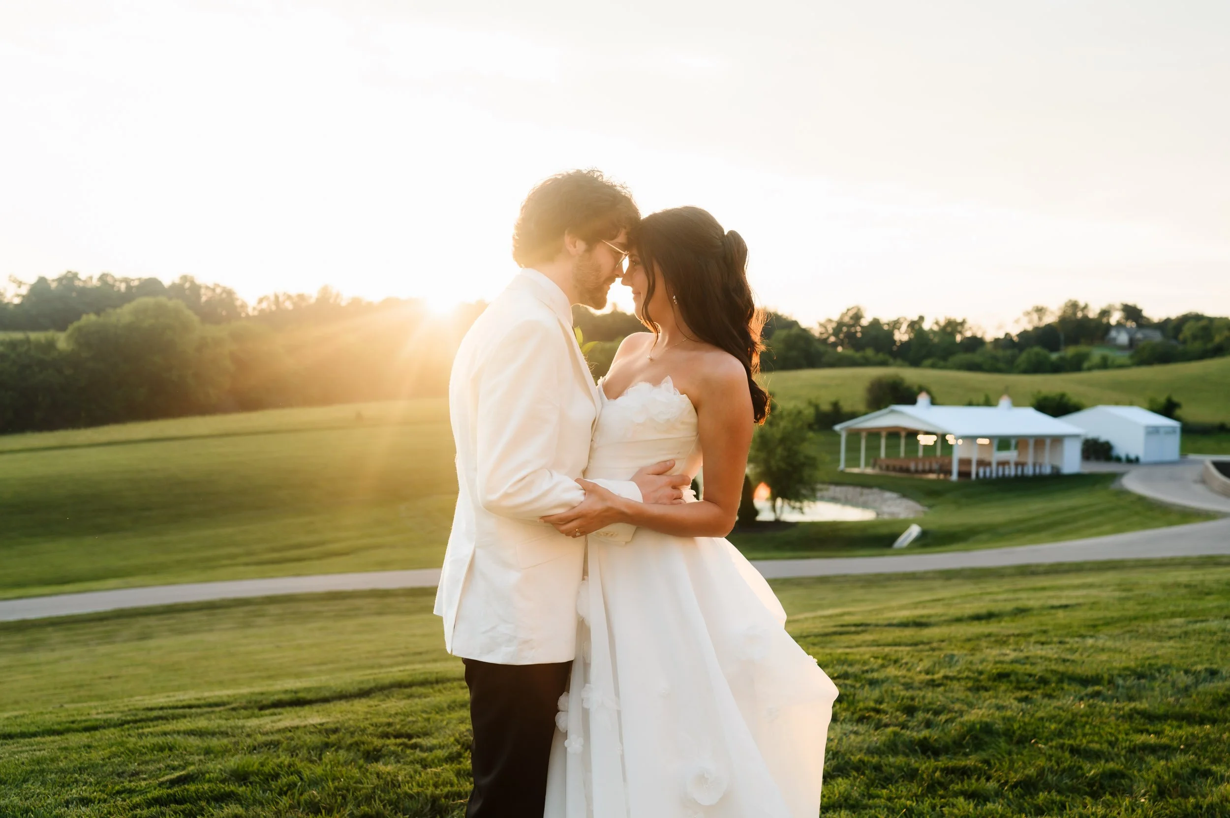 Bride and groom embracing during sunset wedding portraits outdoors at The White Dove Barn