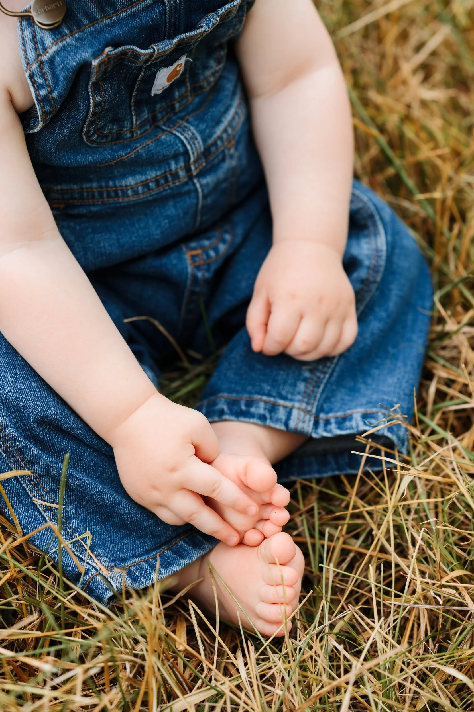 Close-up detail photograph of baby's hands and feet wearing denim overalls outdoors