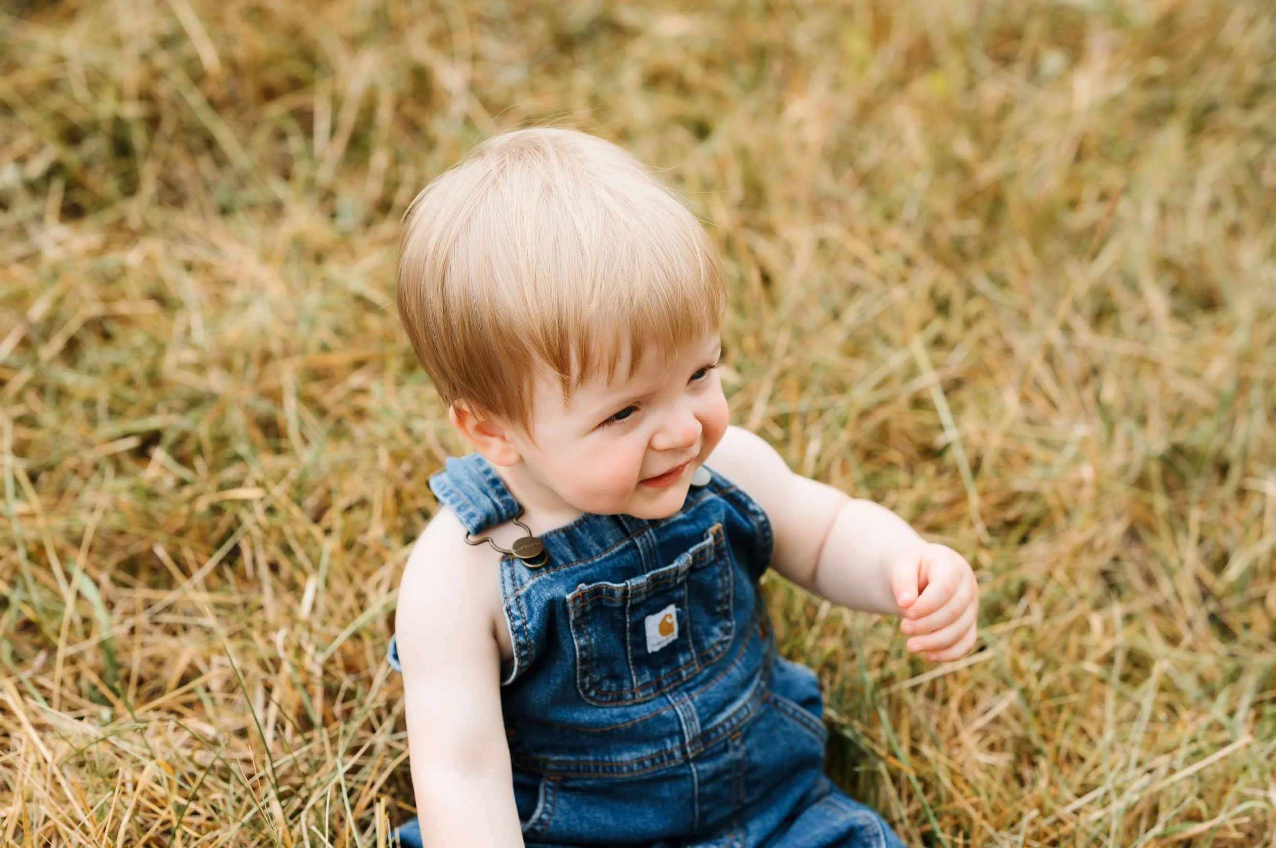Baby boy sitting in grass during outdoor lifestyle birthday session
