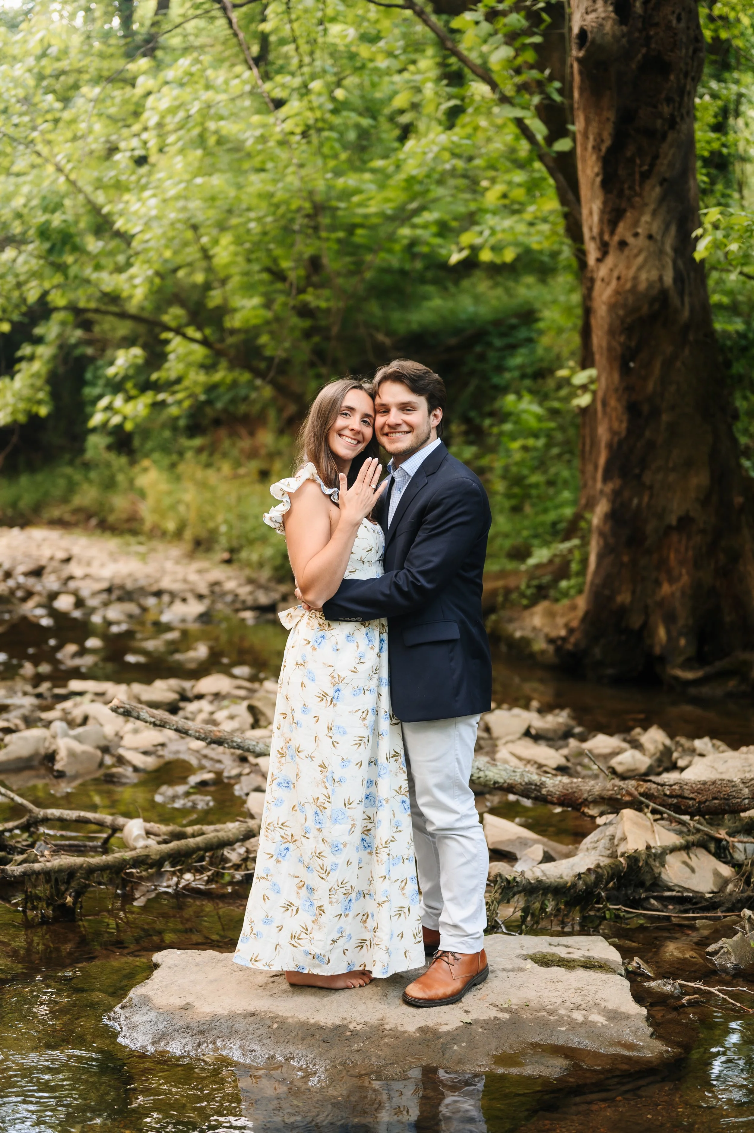 Couple embracing & celebrating engagement proposal beside creek during outdoor portrait session