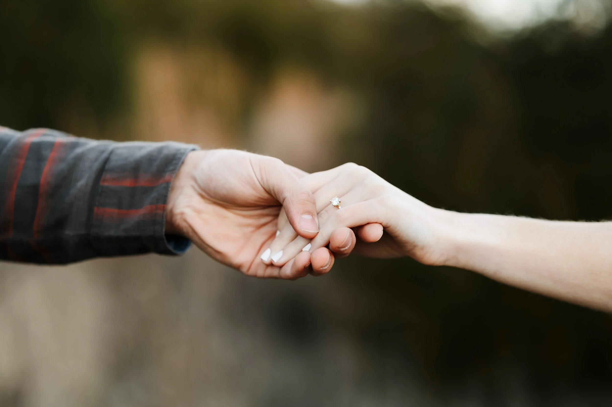 Close-up of couple holding hands and engagement ring outdoors during engagement session