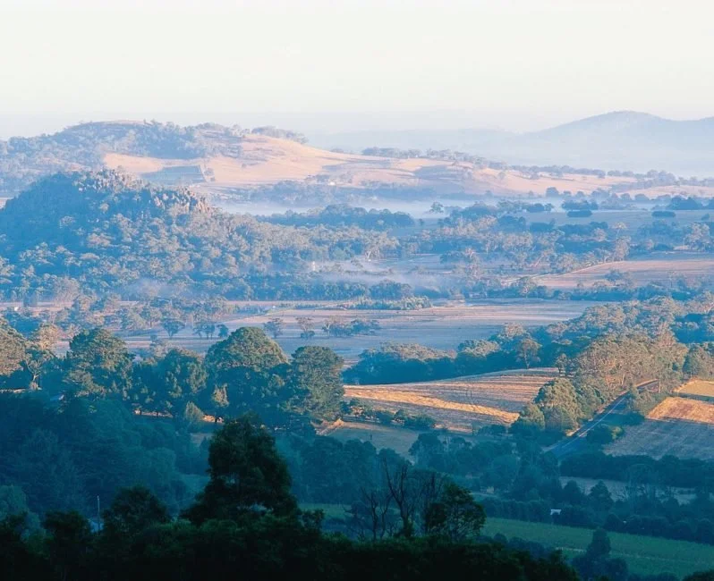 Macedon Ranges and surrounds landscape view of rolling hills, trees, and fields during sunrise or sunset.