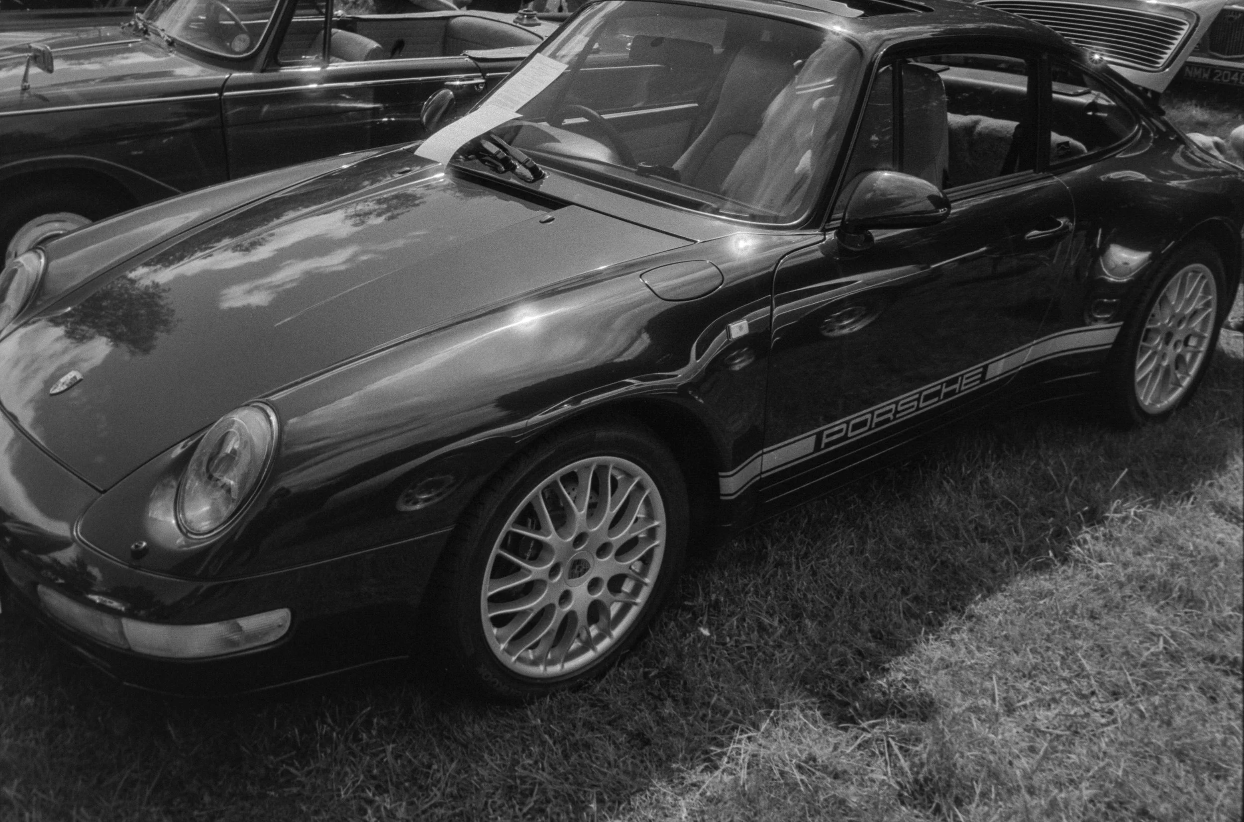 A black Porsche sports car with matching wheels parked on grass at a car show, surrounded by other vintage cars.