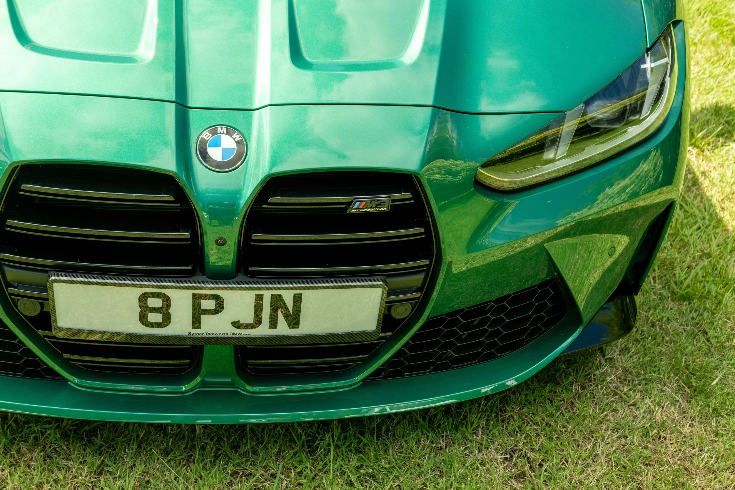 Front view of a bright green BMW sports car with distinctive headlight and grille design, parked on grass, with a visible UK license plate reading '8 PJN'.