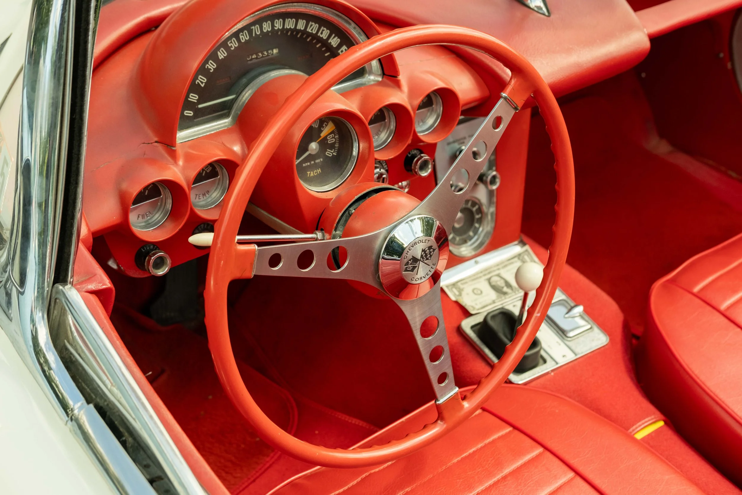 Red vintage Chevrolet Corvette interior with dashboard, steering wheel, and gauges, featuring a tachometer and temperature controls.