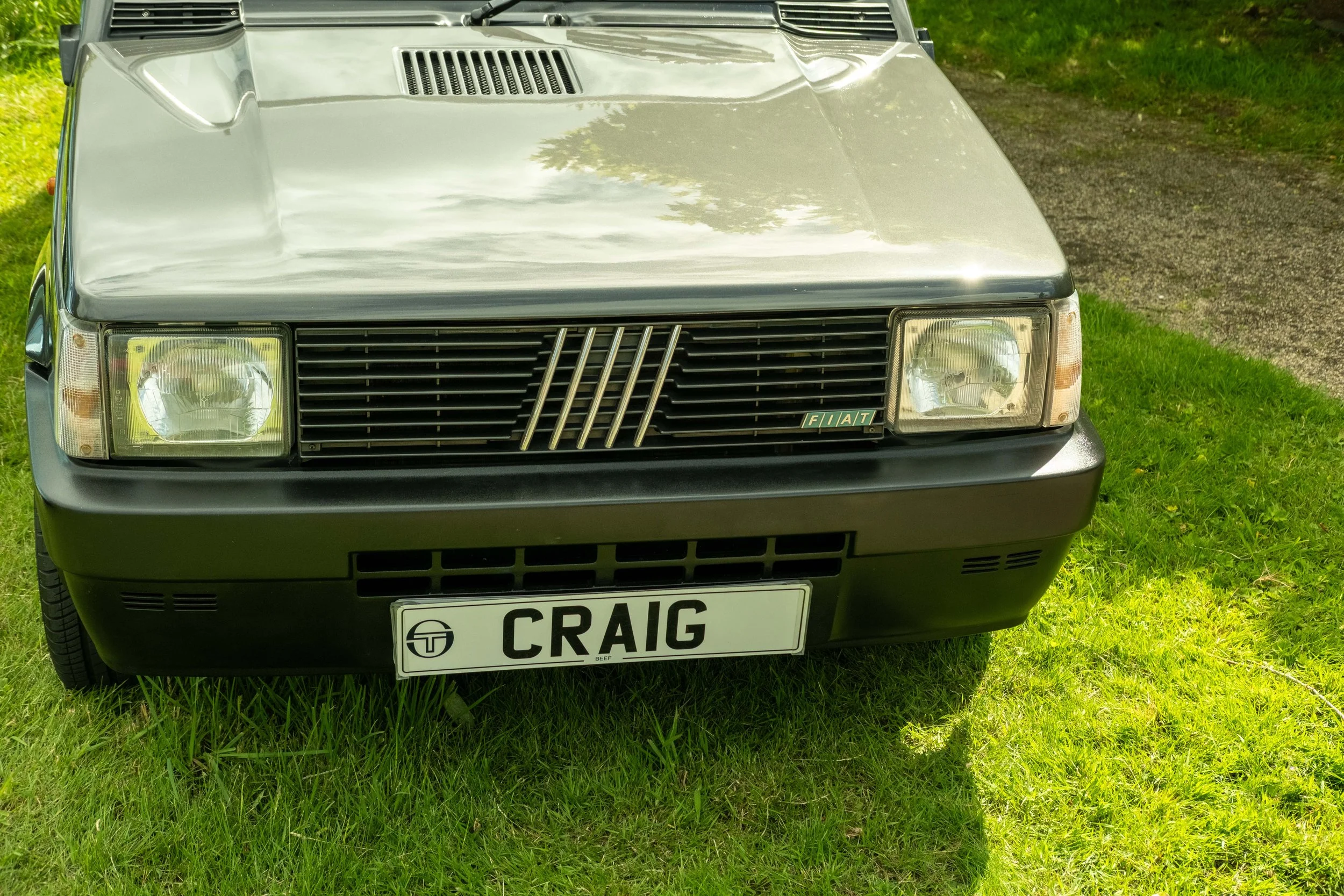 Front view of a classic Fiat car parked on grass, with a personalized license plate reading 'CRAIG' and a black grille.