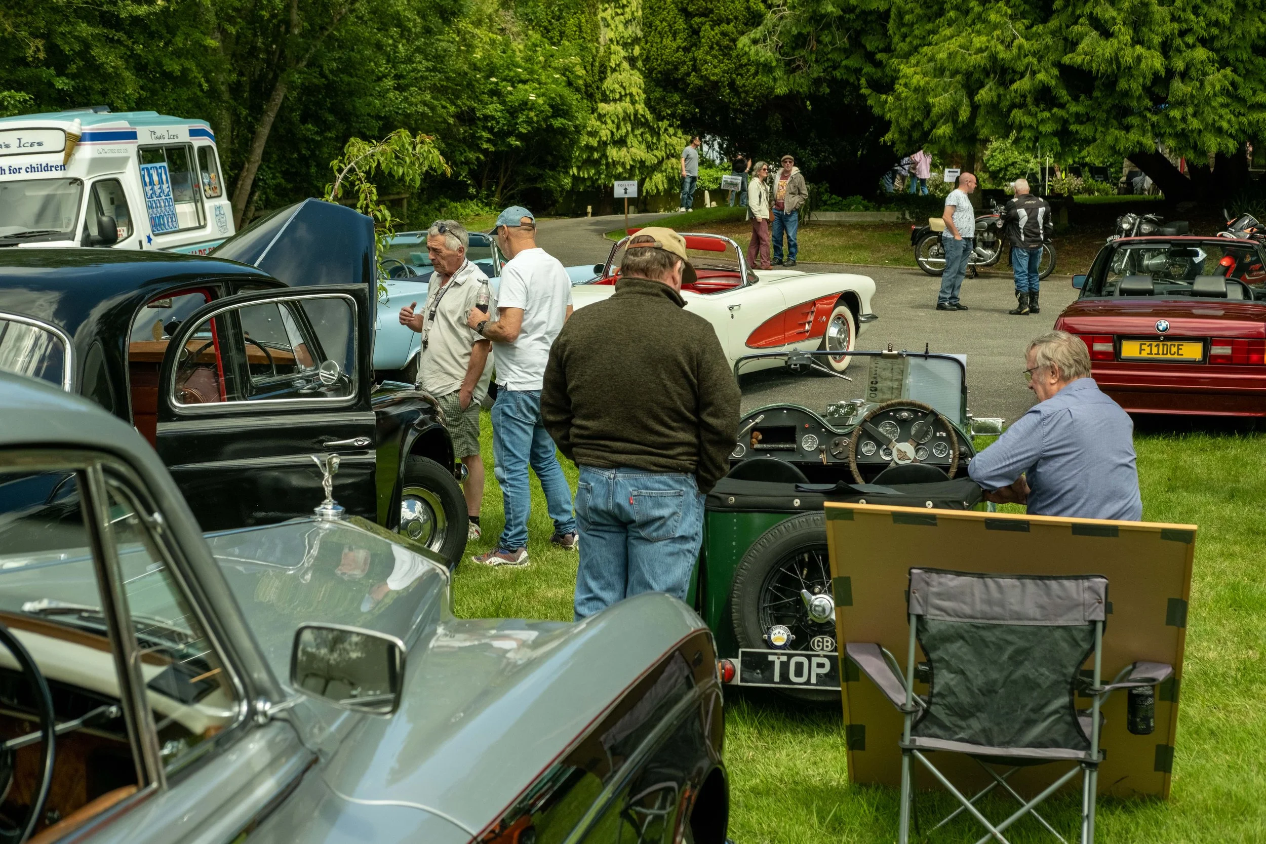 A gathering of people at a classic car show with vintage cars and motorcycles on display in a park setting.