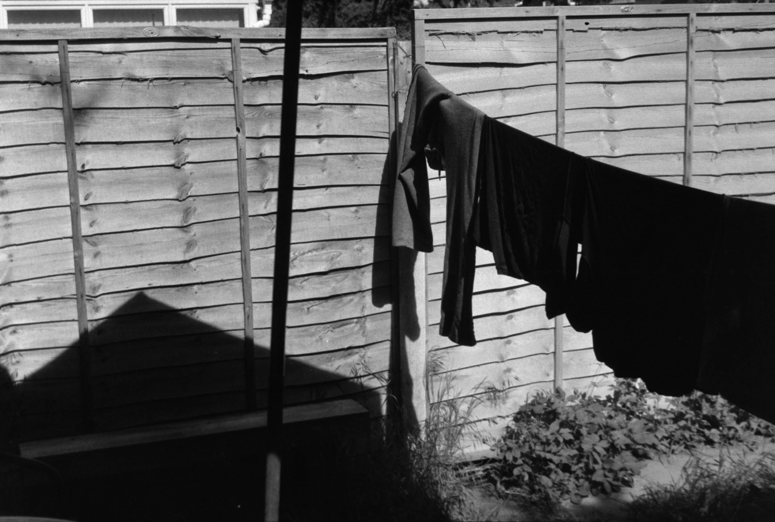 Black and white photo of laundry hanging on a clothesline in front of a wooden fence.