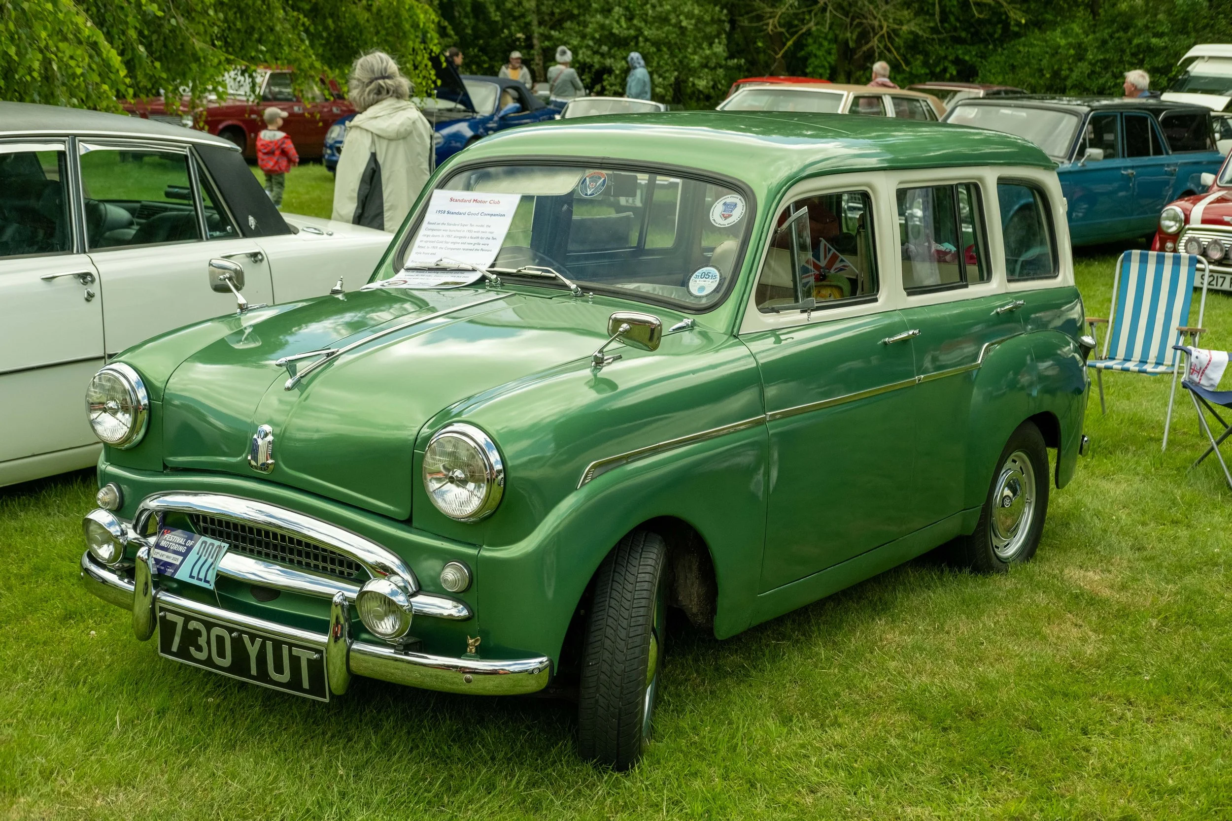 A vintage green and white car at a classic car show on a grassy field, with several other vintage cars and people in the background.