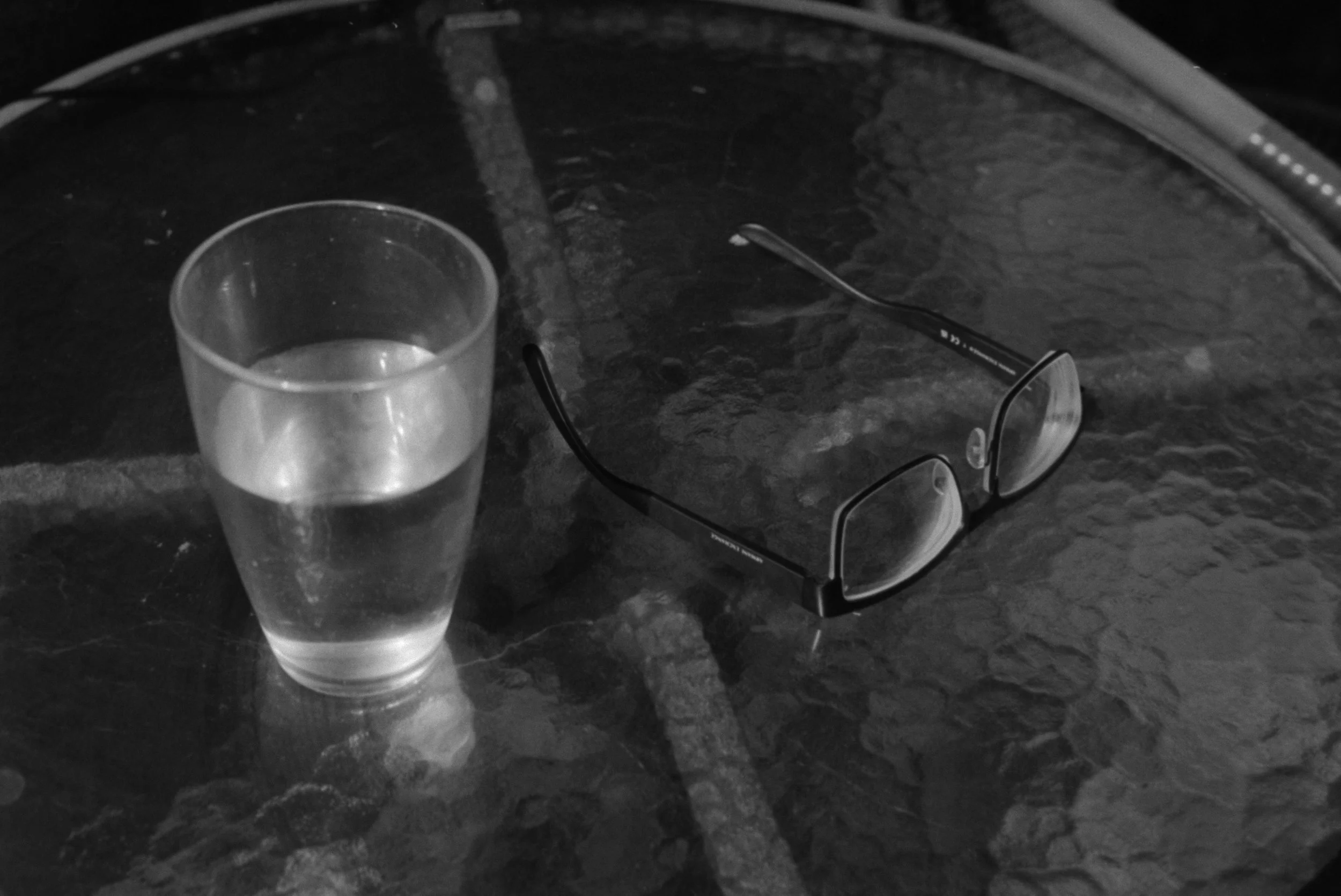 A glass of water and a pair of eyeglasses resting on a dark marble table.
