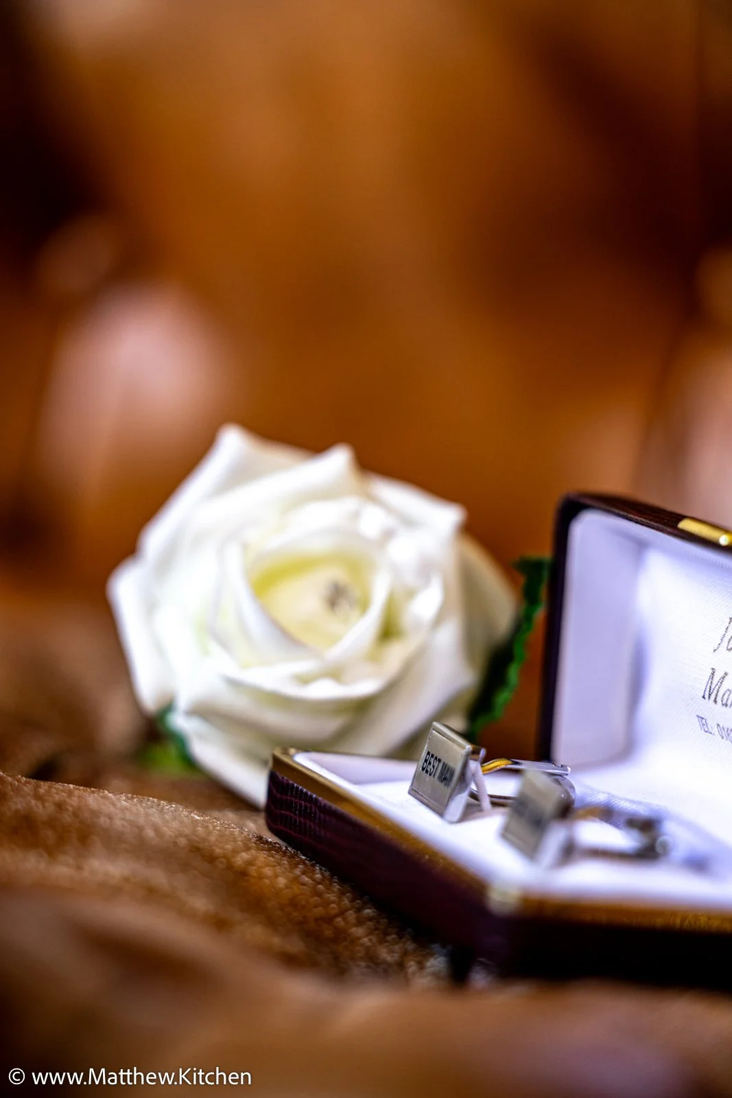 A white rose and a pair of cufflinks in a display box, with an out-of-focus background.