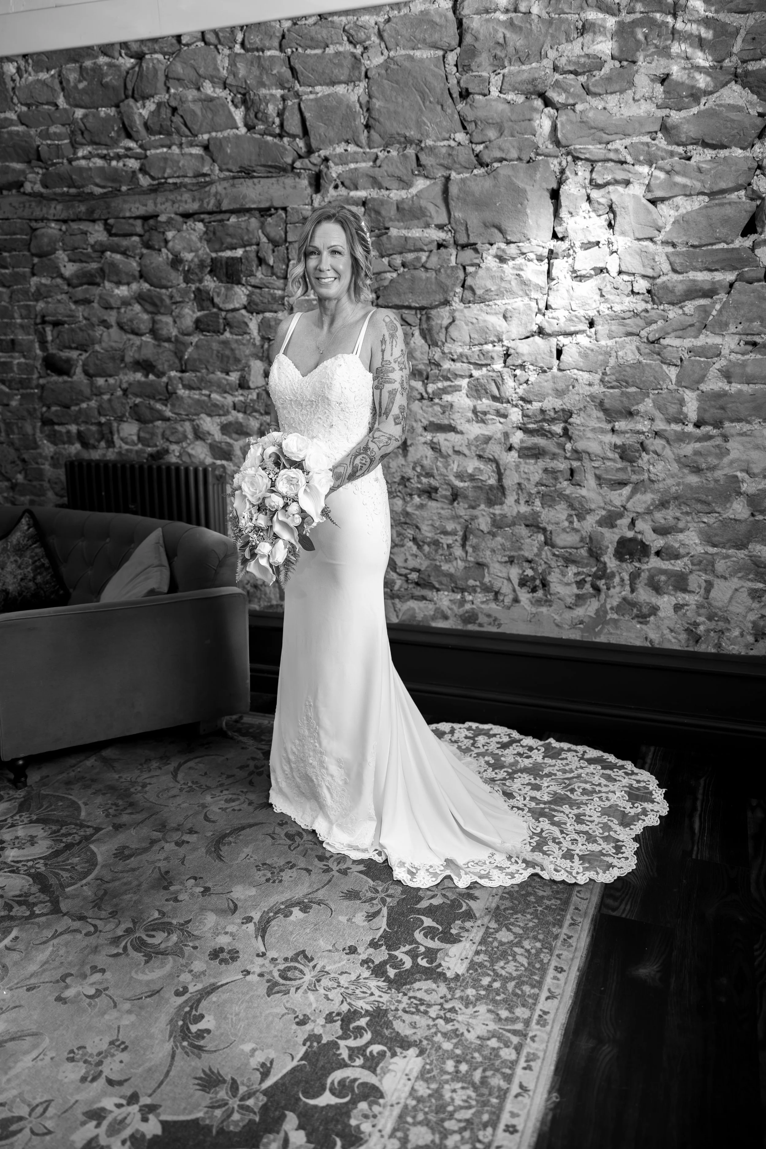 A bride in a wedding dress holding a bouquet of flowers, standing in front of a textured stone wall.