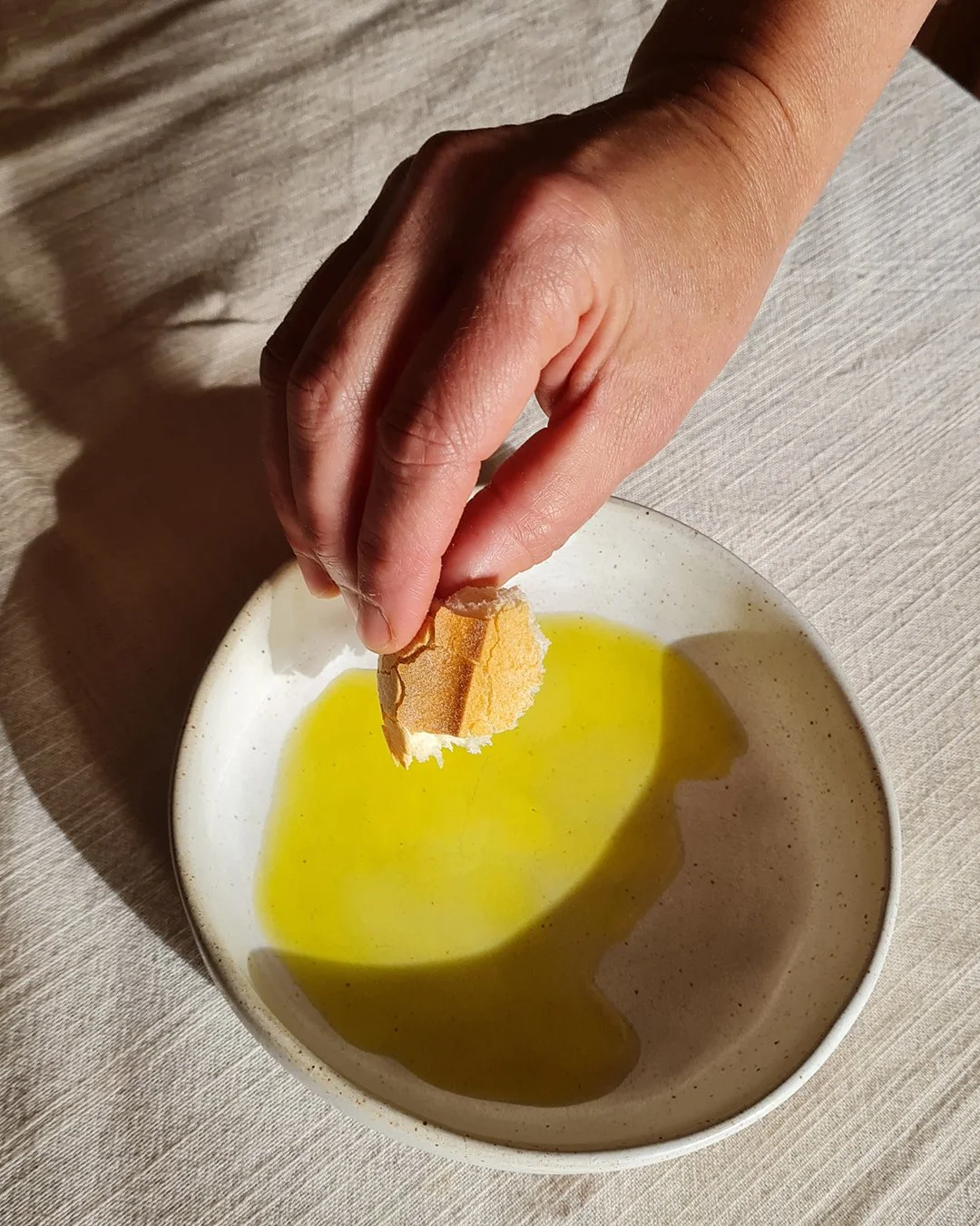 mano con un trozo de pan y un plato con aceite de olivaplato